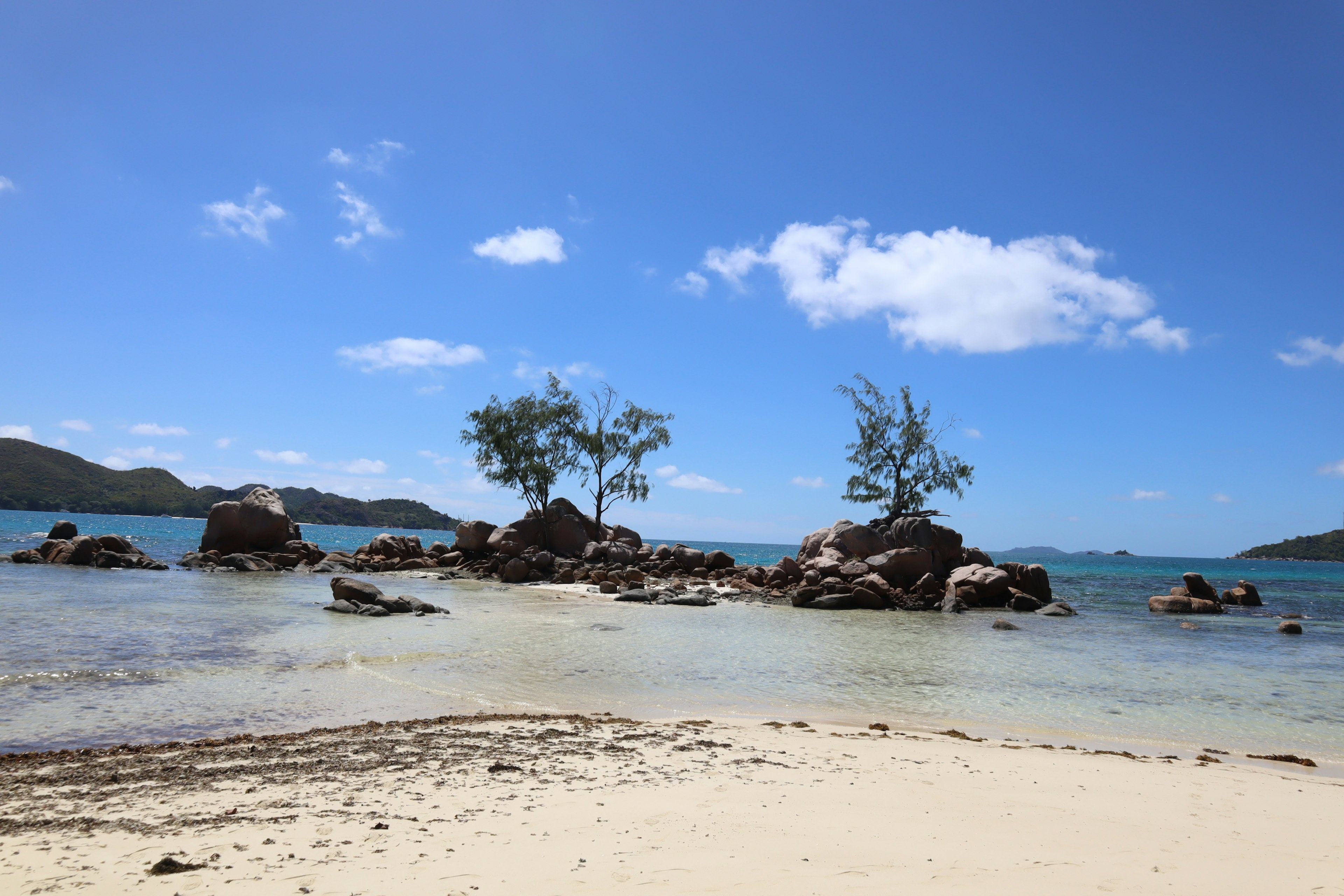 Beach scene with small island and rocks under a blue sky