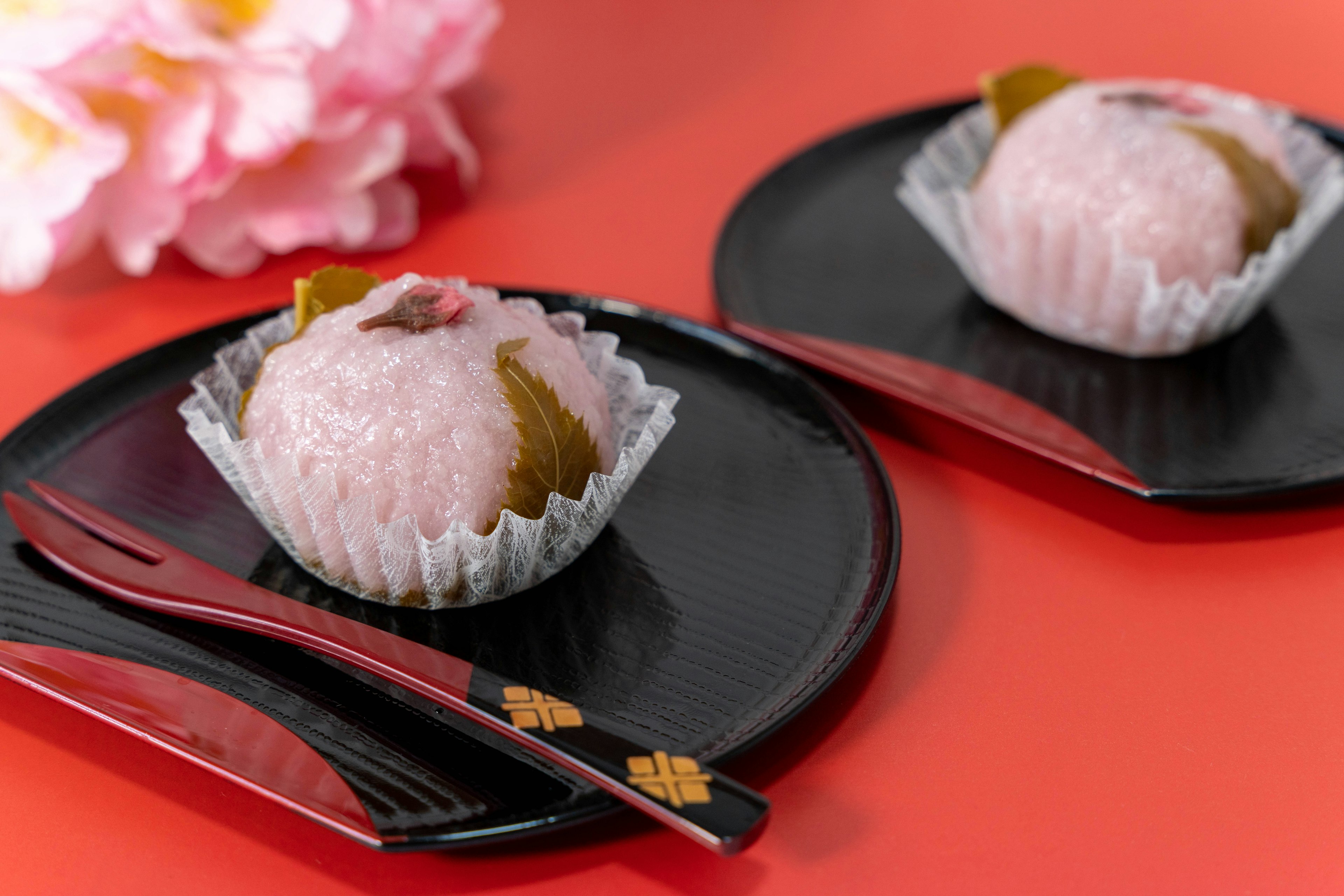 Kue Jepang berwarna pink dibungkus daun sakura di piring hitam