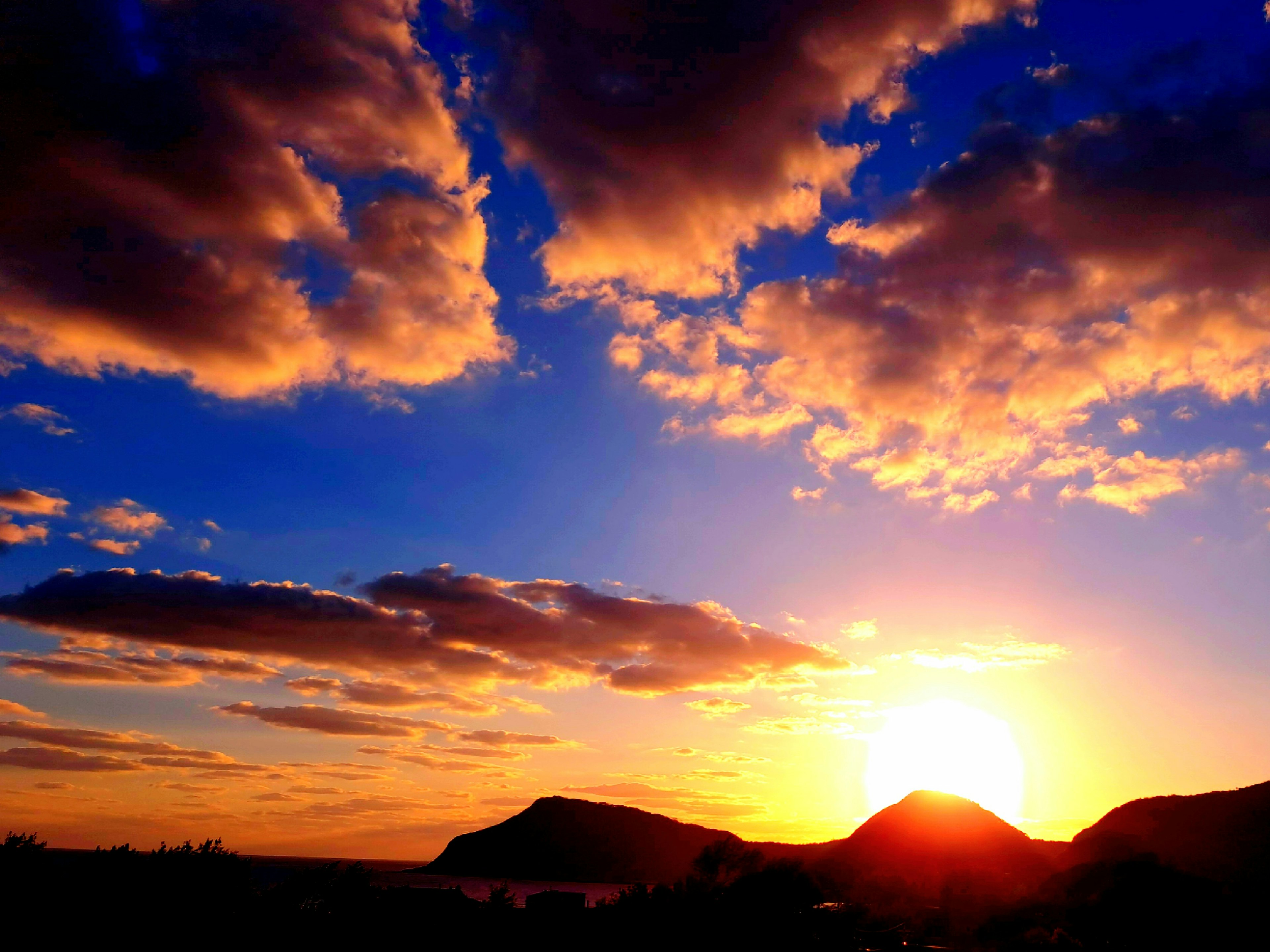 Hermoso paisaje de un atardecer con nubes naranjas y cielo azul, siluetas de montañas