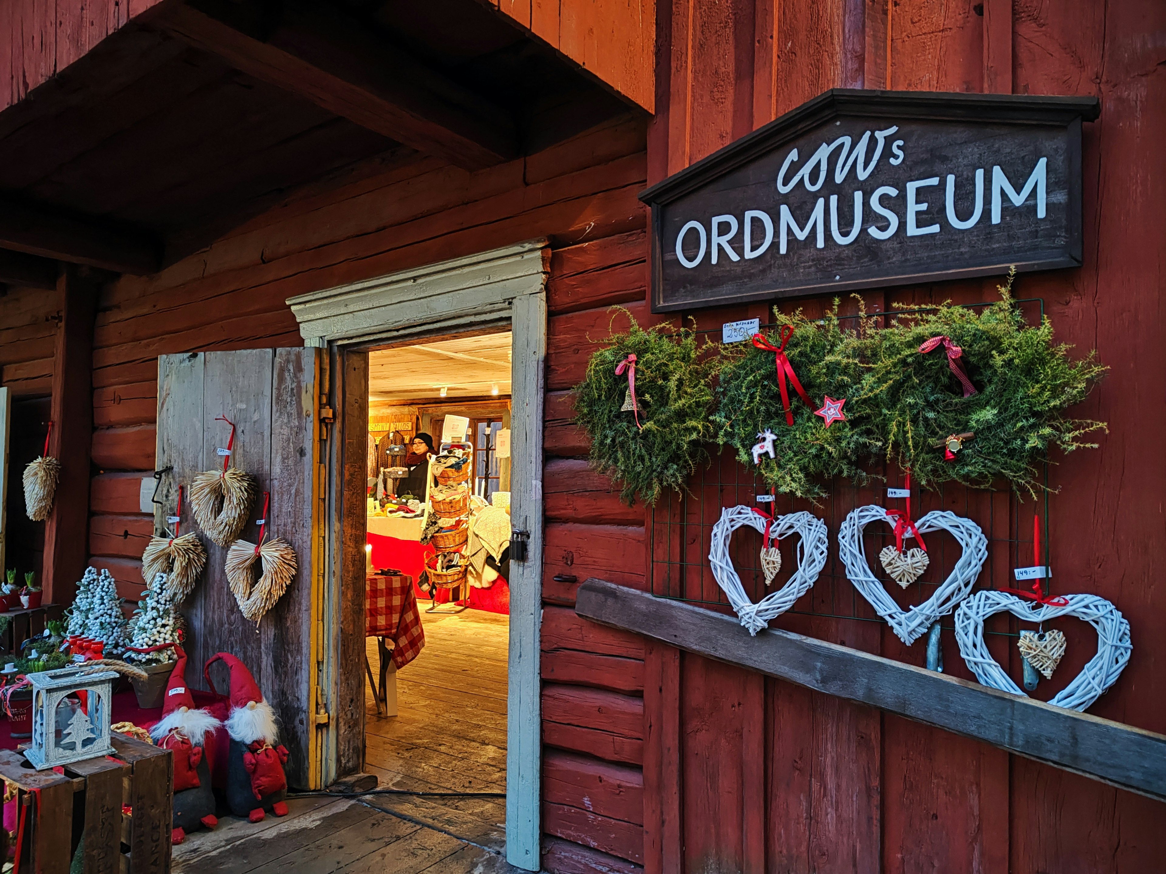 Entrada de una cabaña de madera roja con coronas en forma de corazón y un letrero del museo Cow's Ord