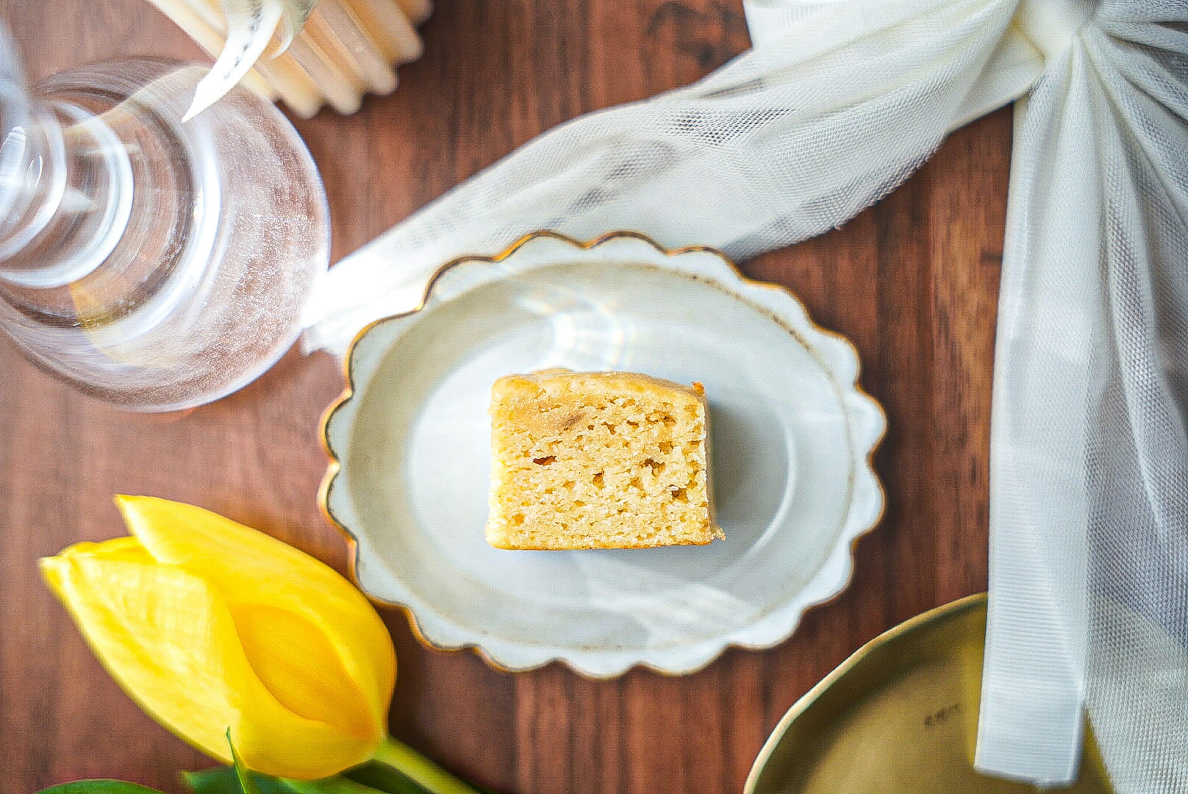 A slice of cake on a decorative plate with a yellow tulip nearby