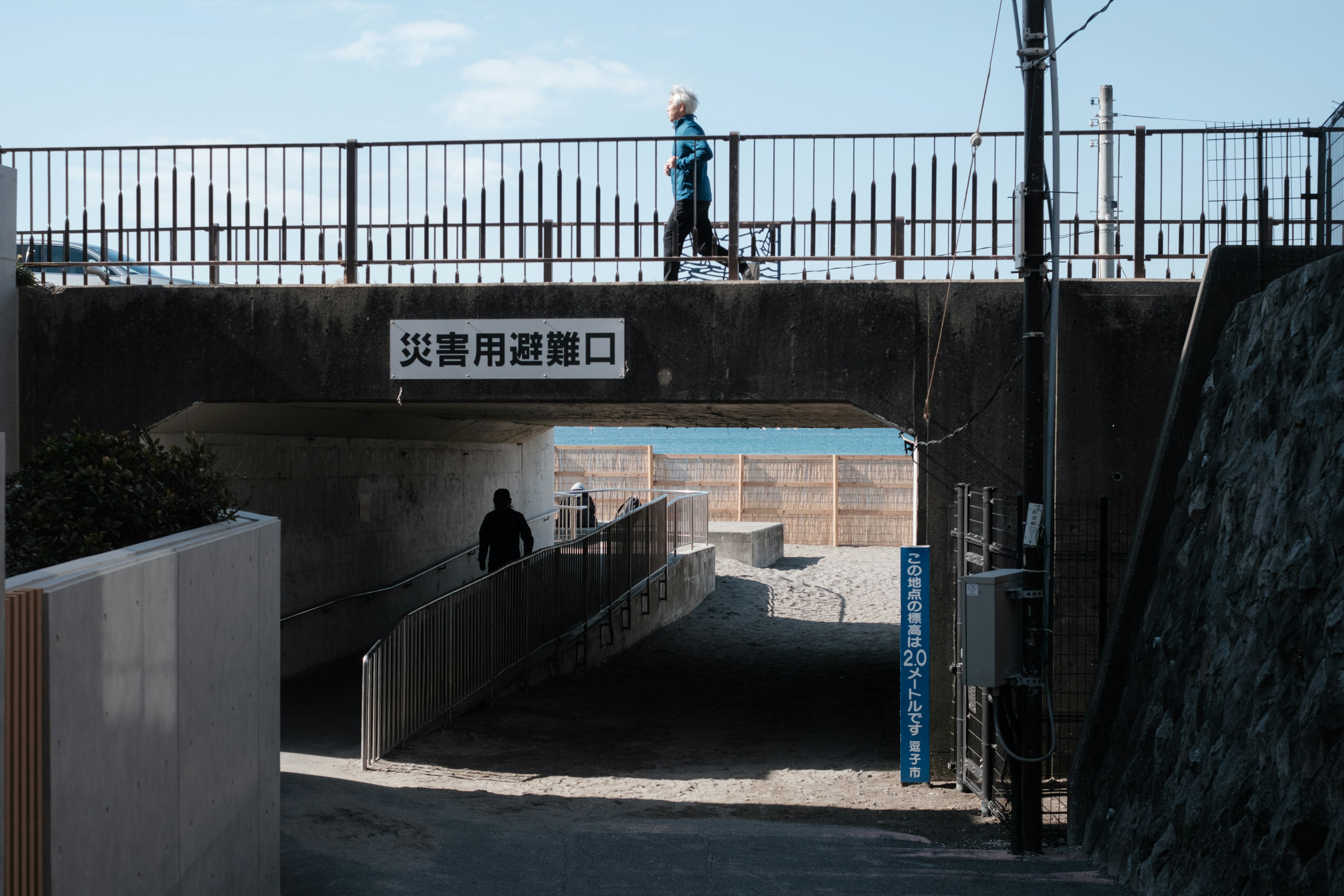 A person in blue walking on an overpass with a view of the ocean