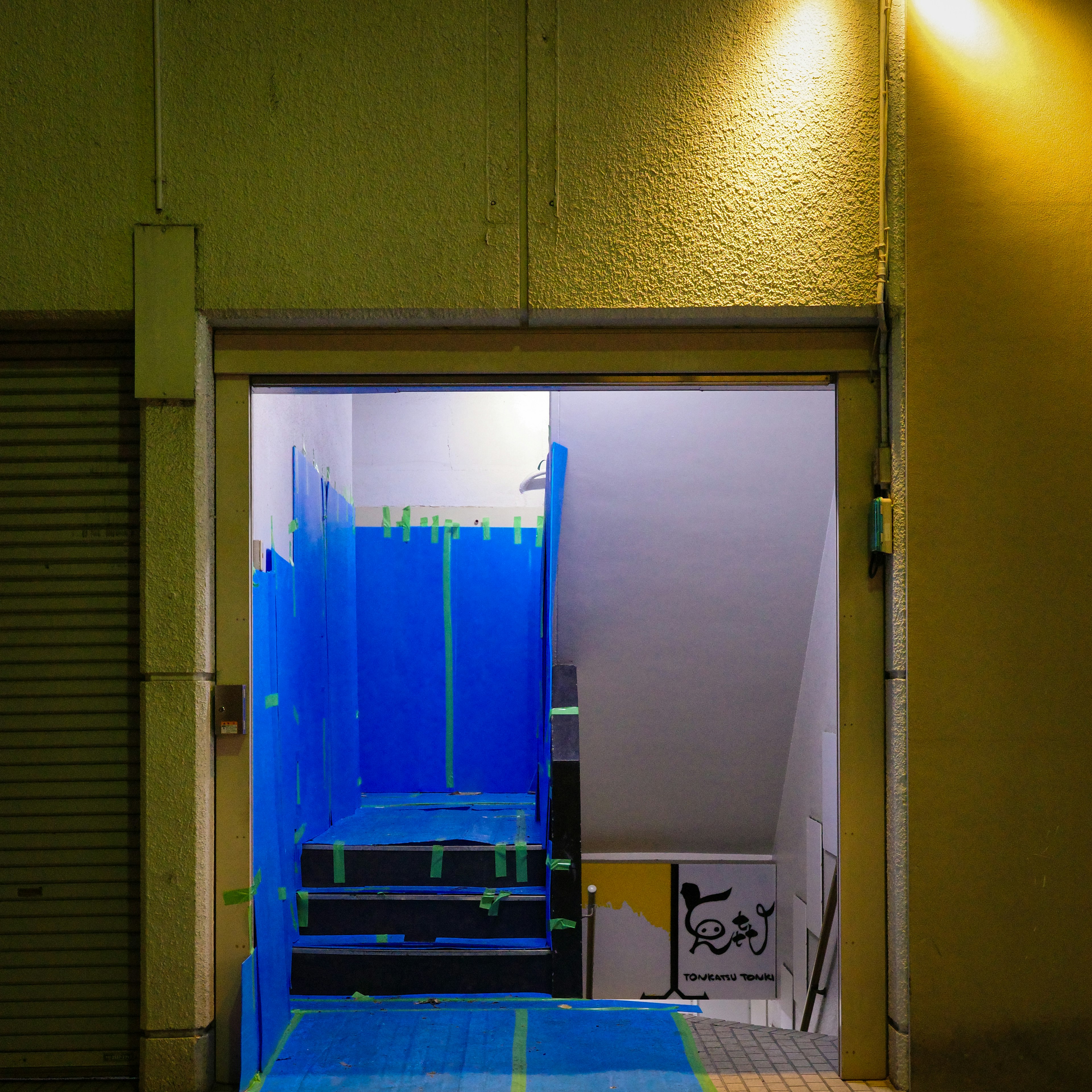 Entrada que muestra una escalera cubierta con cinta azul en un pasillo poco iluminado