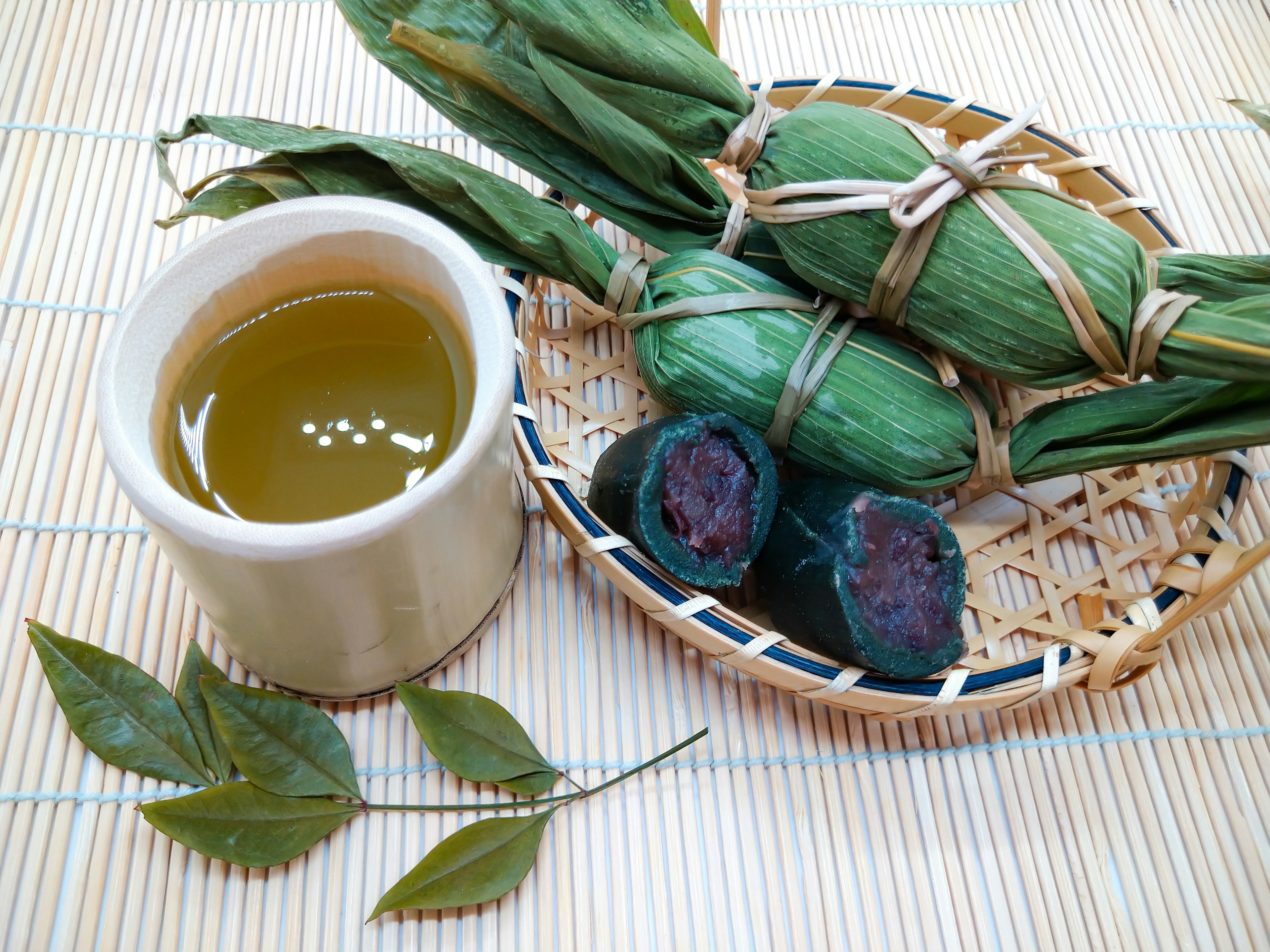 Gambar yang menampilkan makanan dibungkus daun hijau bersama secangkir teh