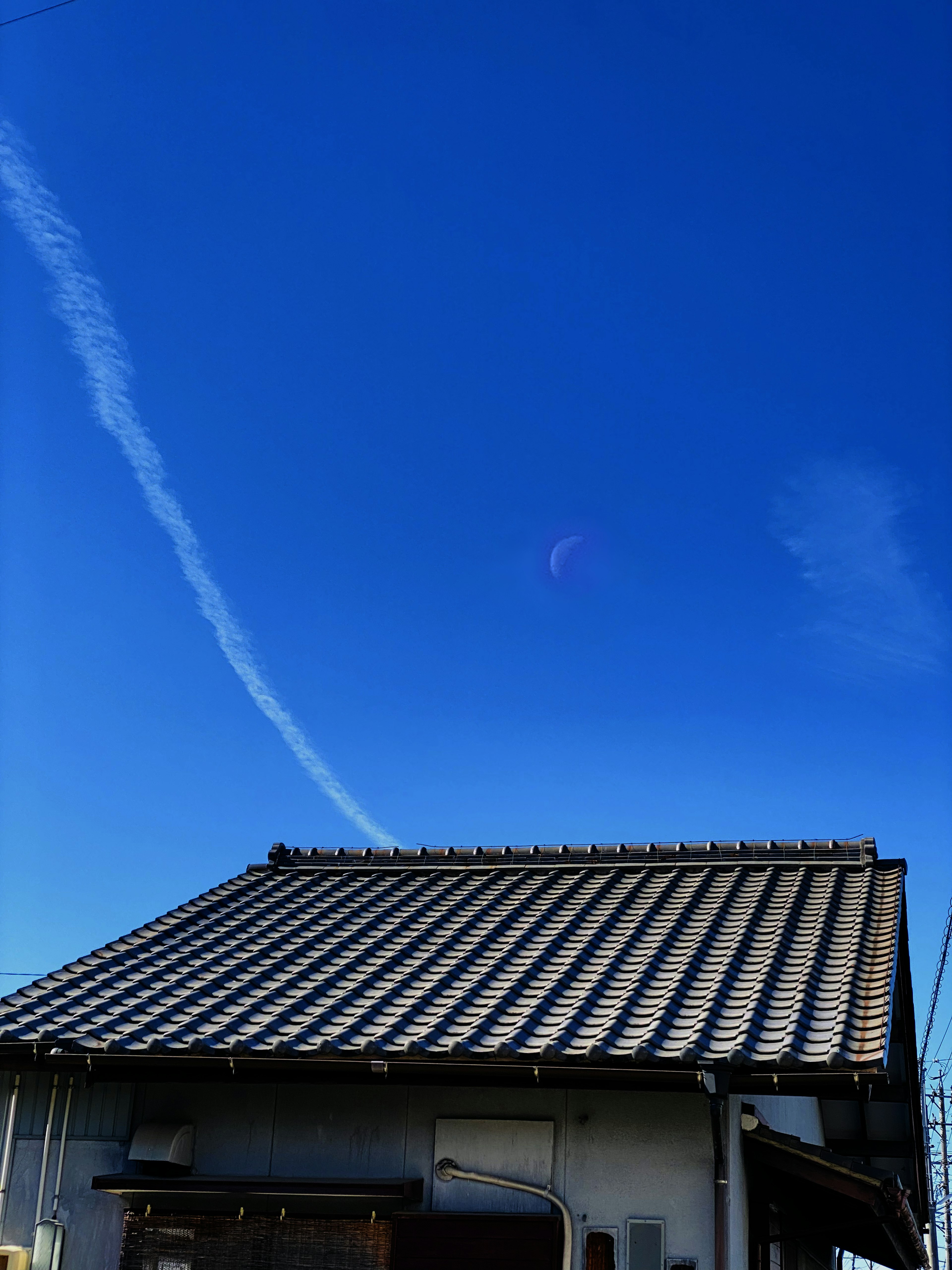 青空に白い飛行機雲が見える日本の伝統的な屋根の家