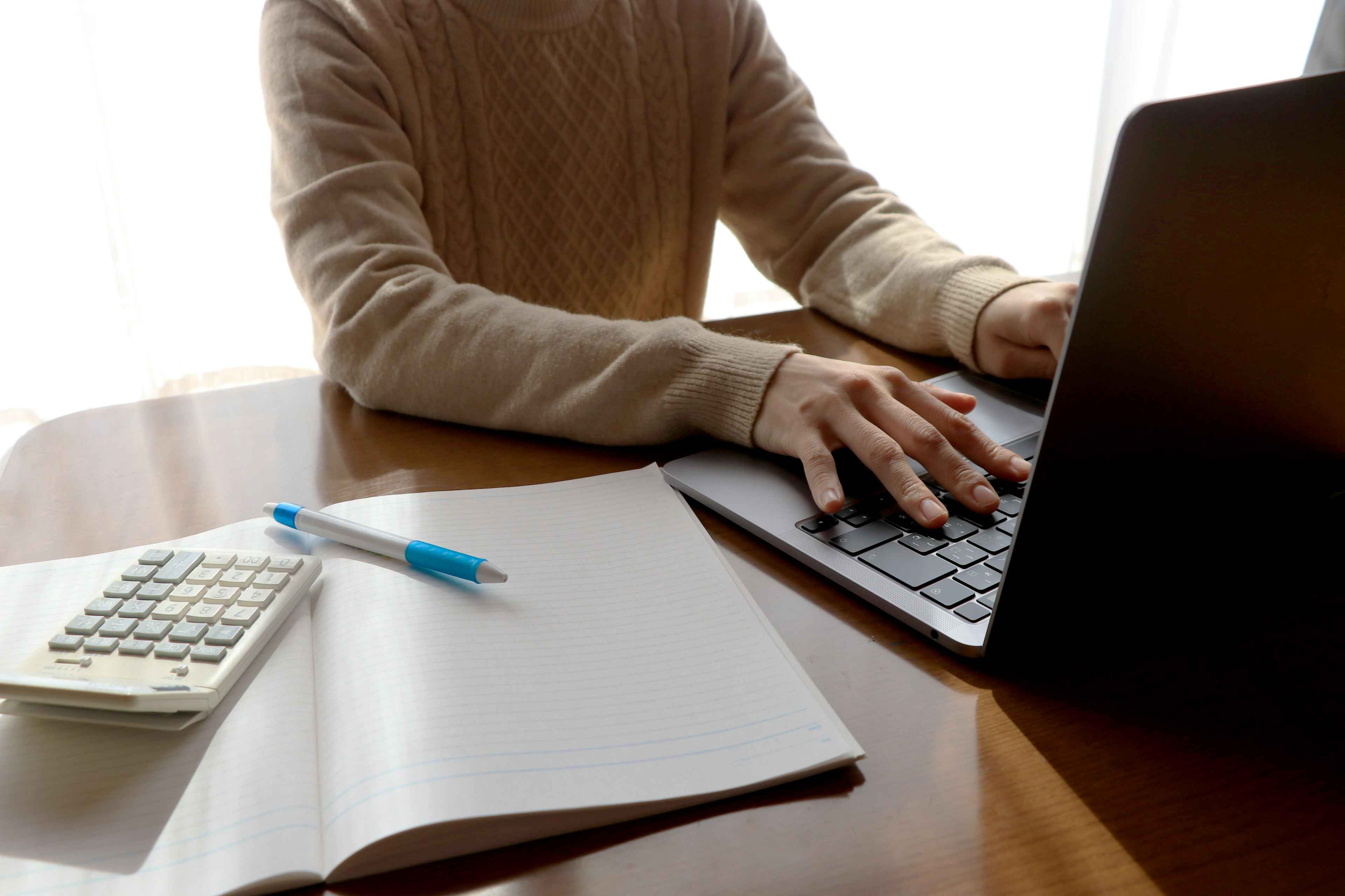 Gros plan sur des mains tapant sur un ordinateur portable à un bureau avec une calculatrice un stylo bleu et un carnet blanc