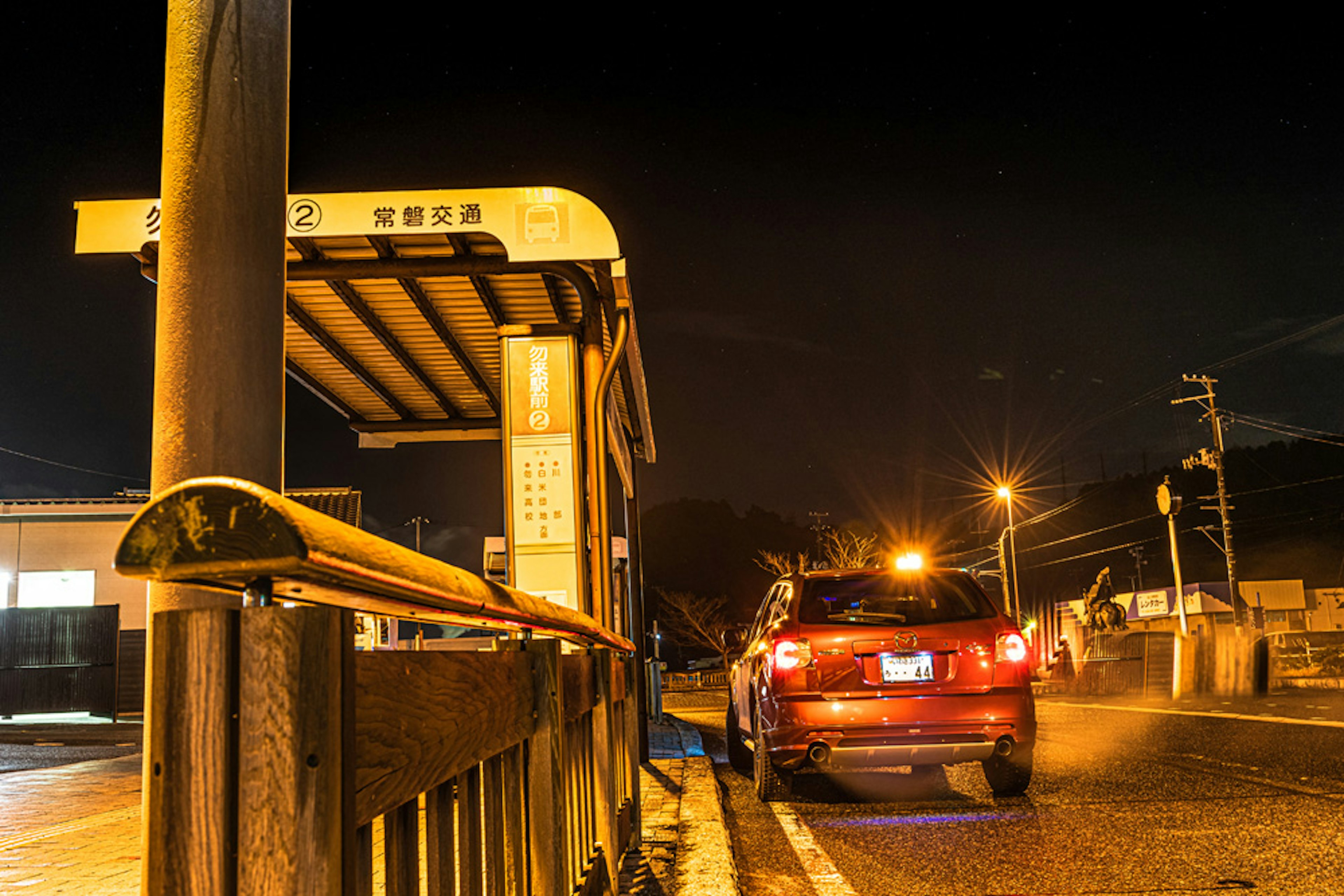 Night scene of a bus stop with a red car