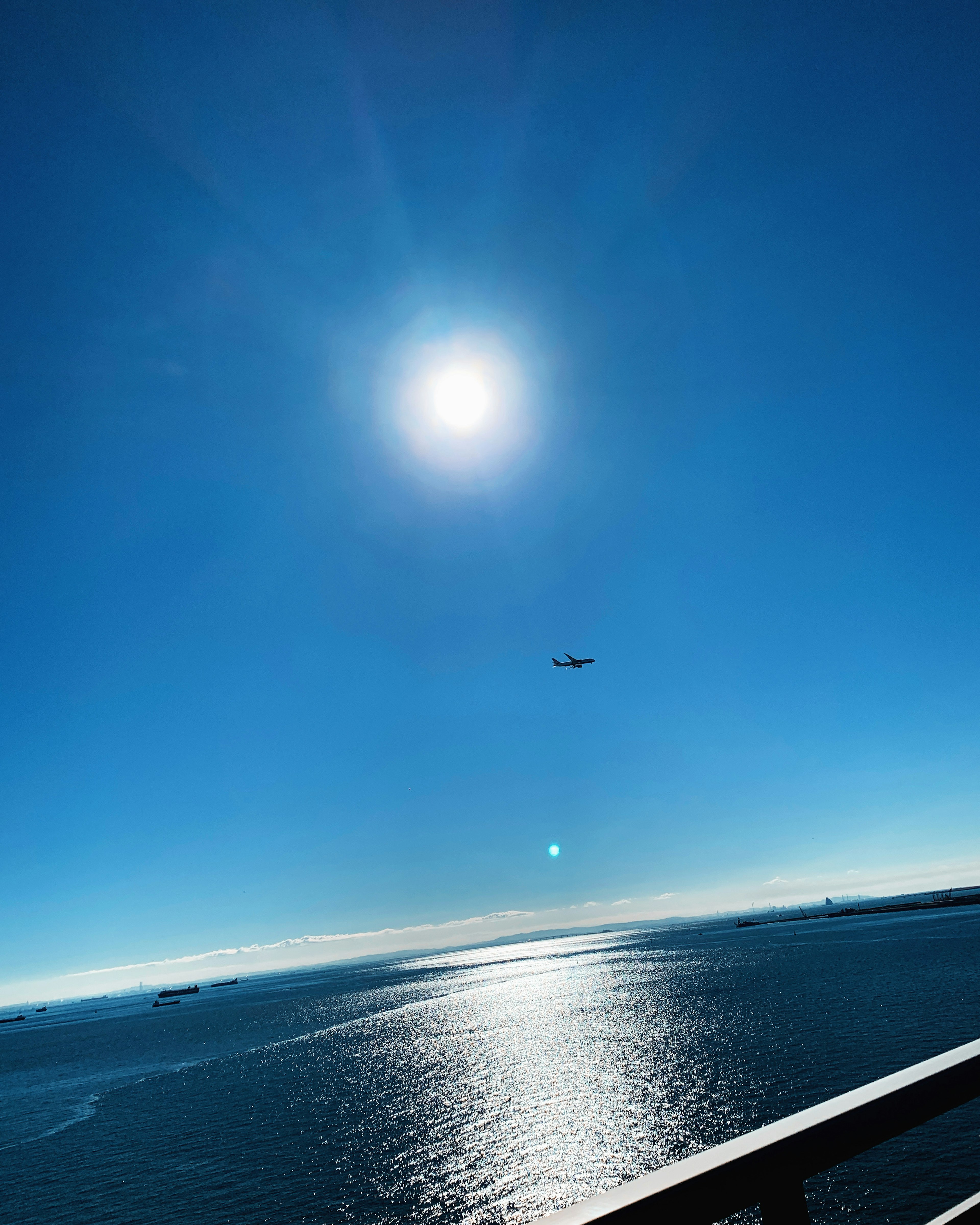 Ein strahlend blauer Himmel mit der Sonne, die über den Ozean scheint, und einem fliegenden Flugzeug