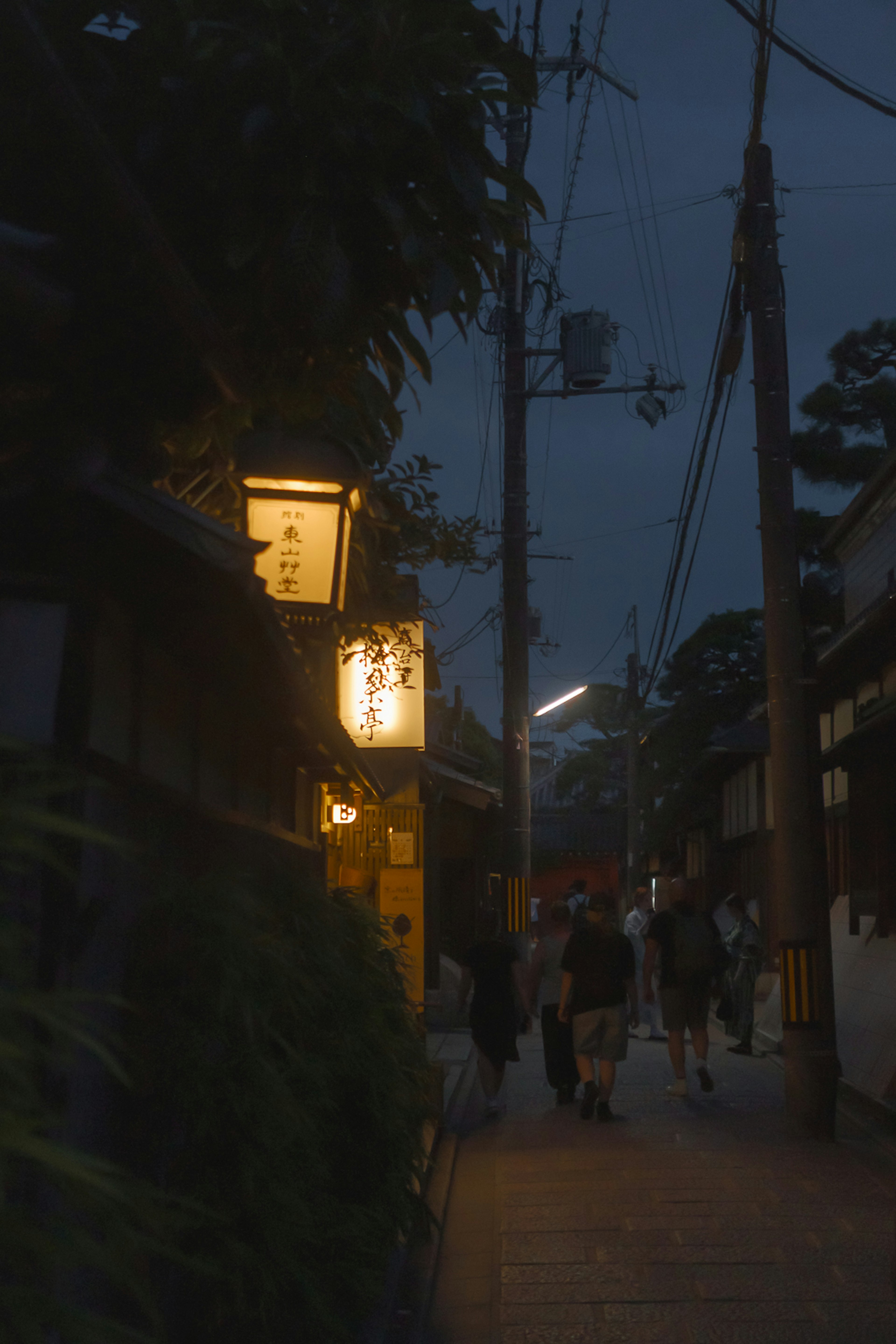 Strada poco illuminata con un'insegna luminosa e persone che camminano