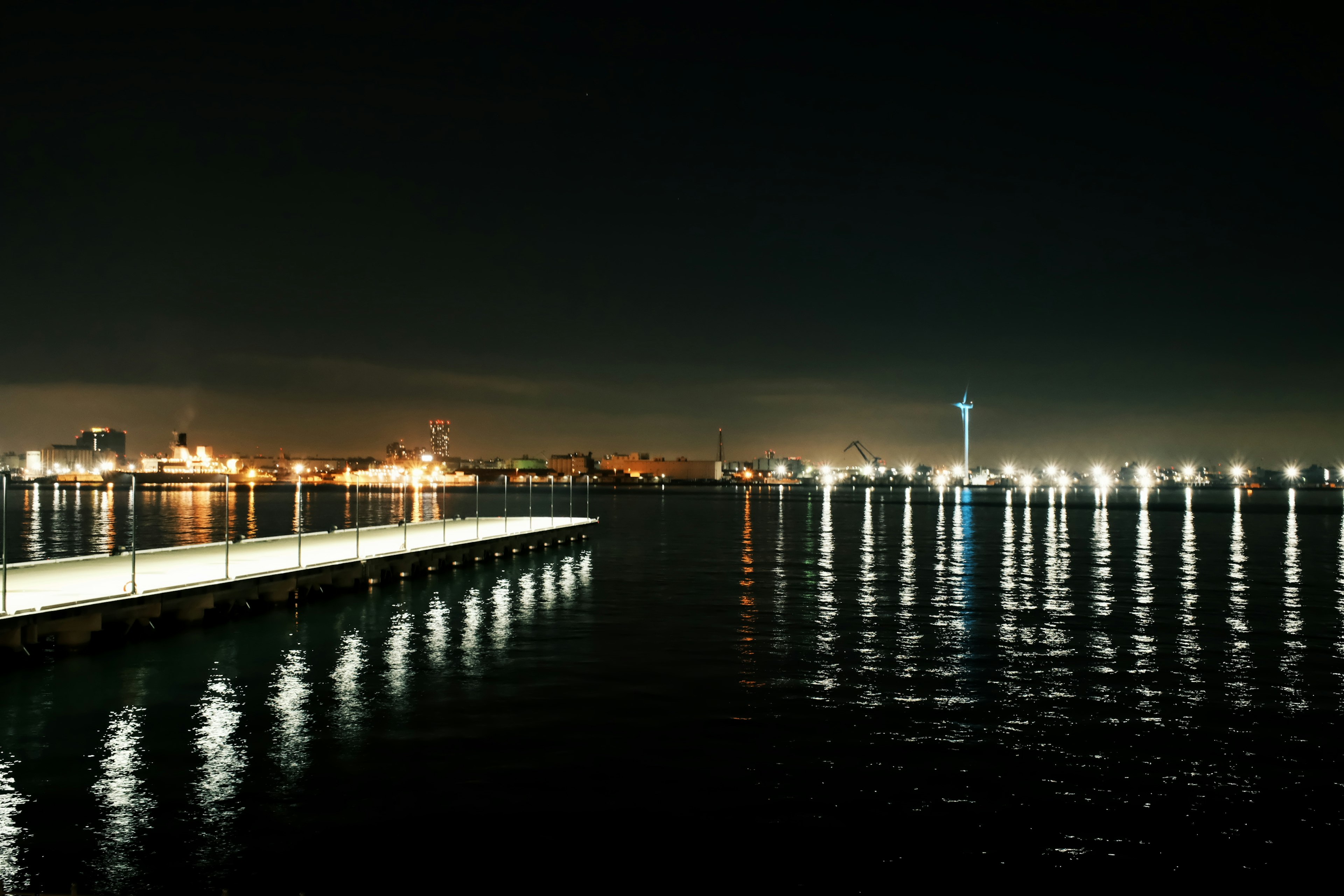 Night view of a pier with reflections on the water and city lights