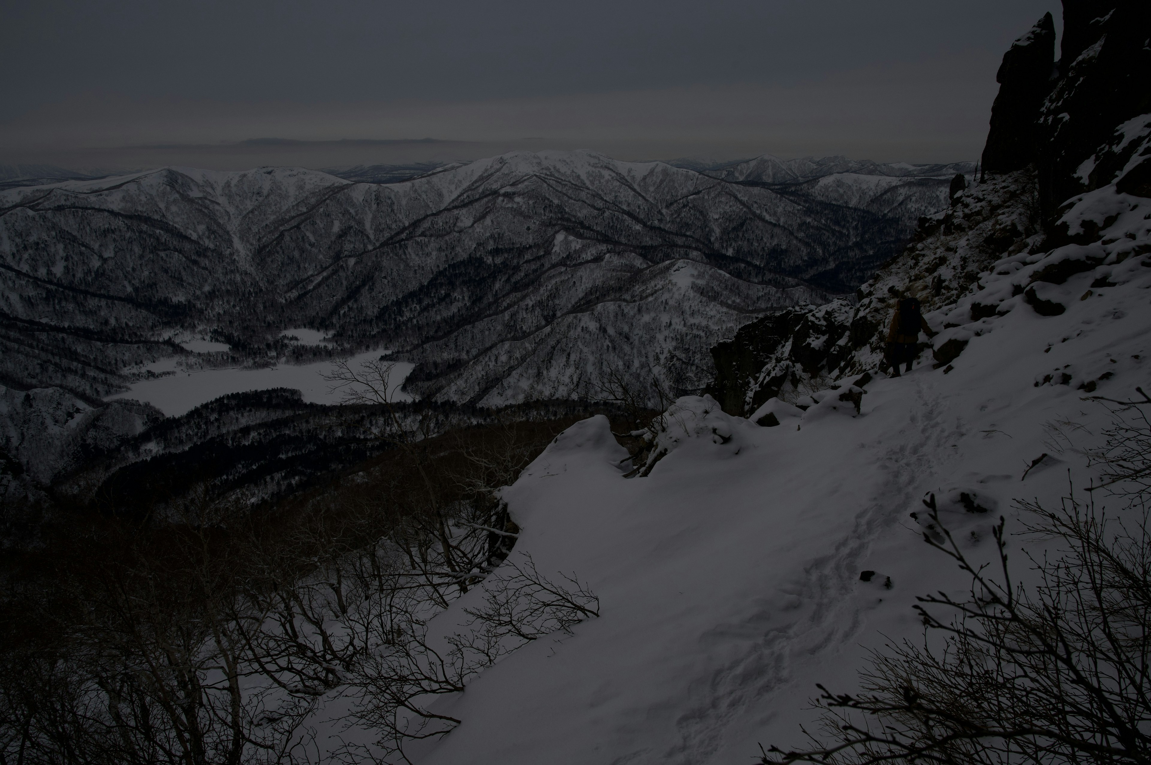 雪に覆われた山々と谷の風景が広がる暗い空の下