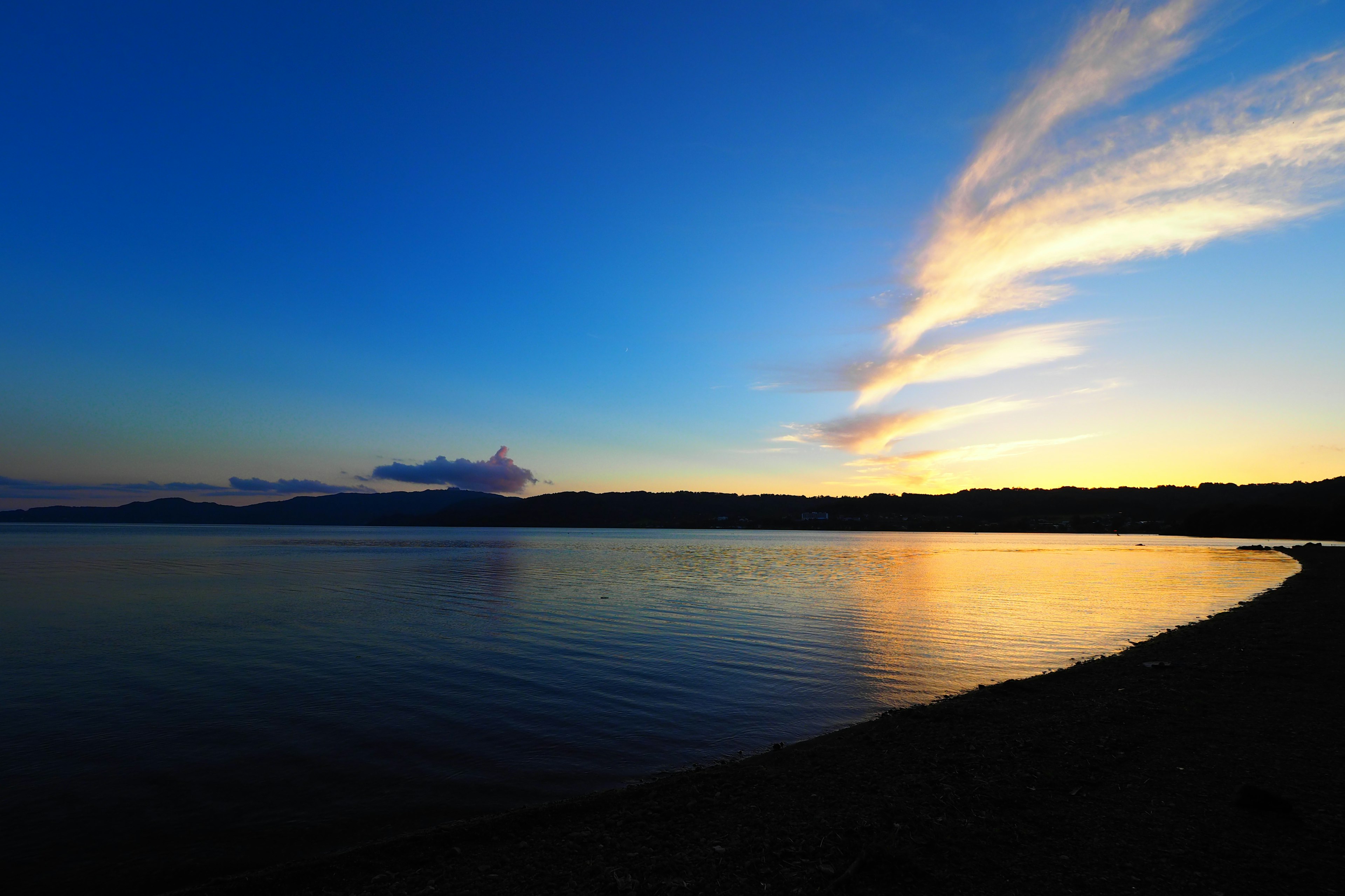 Escena de lago tranquilo con cielo azul y nubes naranjas al atardecer