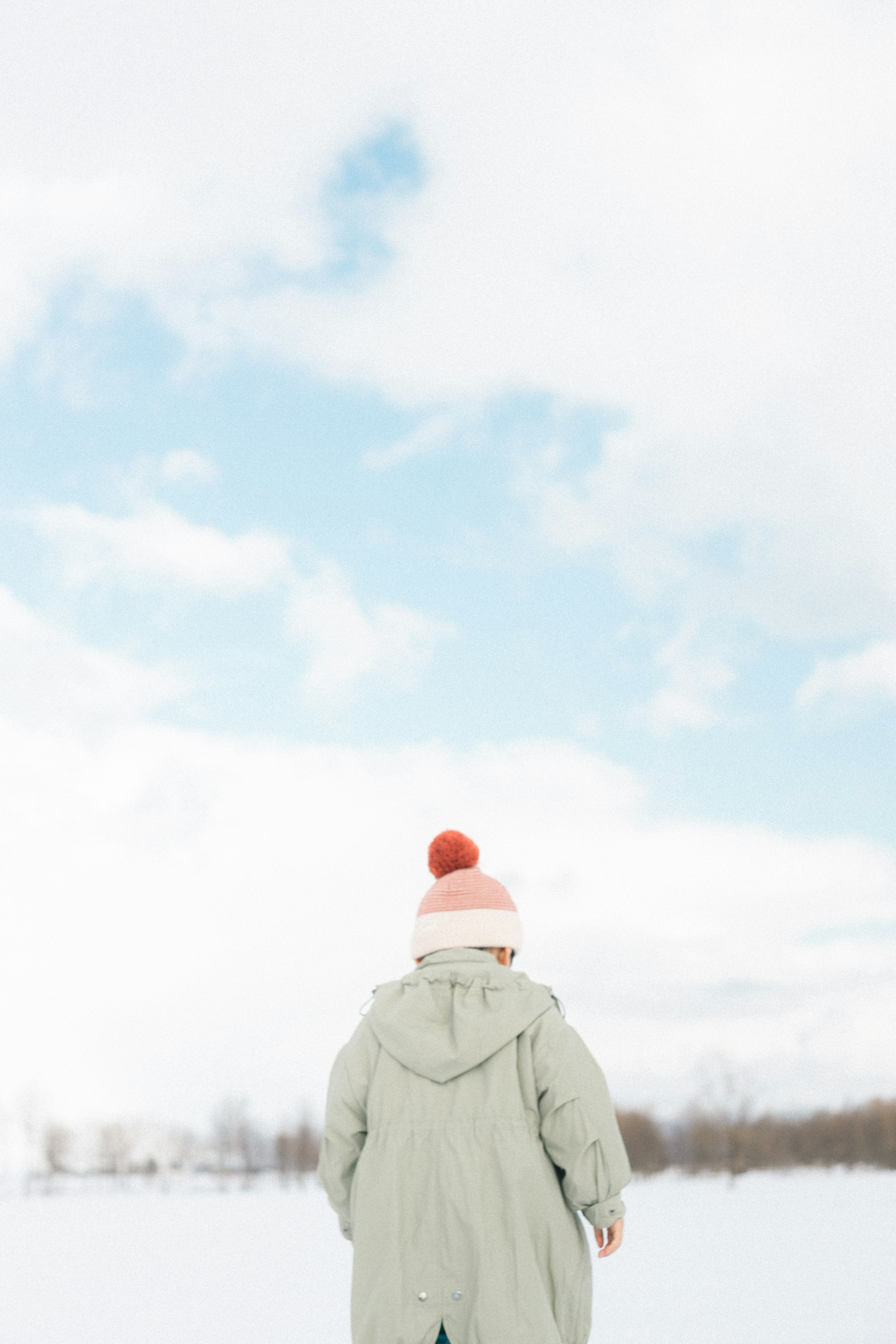 Enfant de dos dans un paysage enneigé avec un manteau vert et un chapeau rose