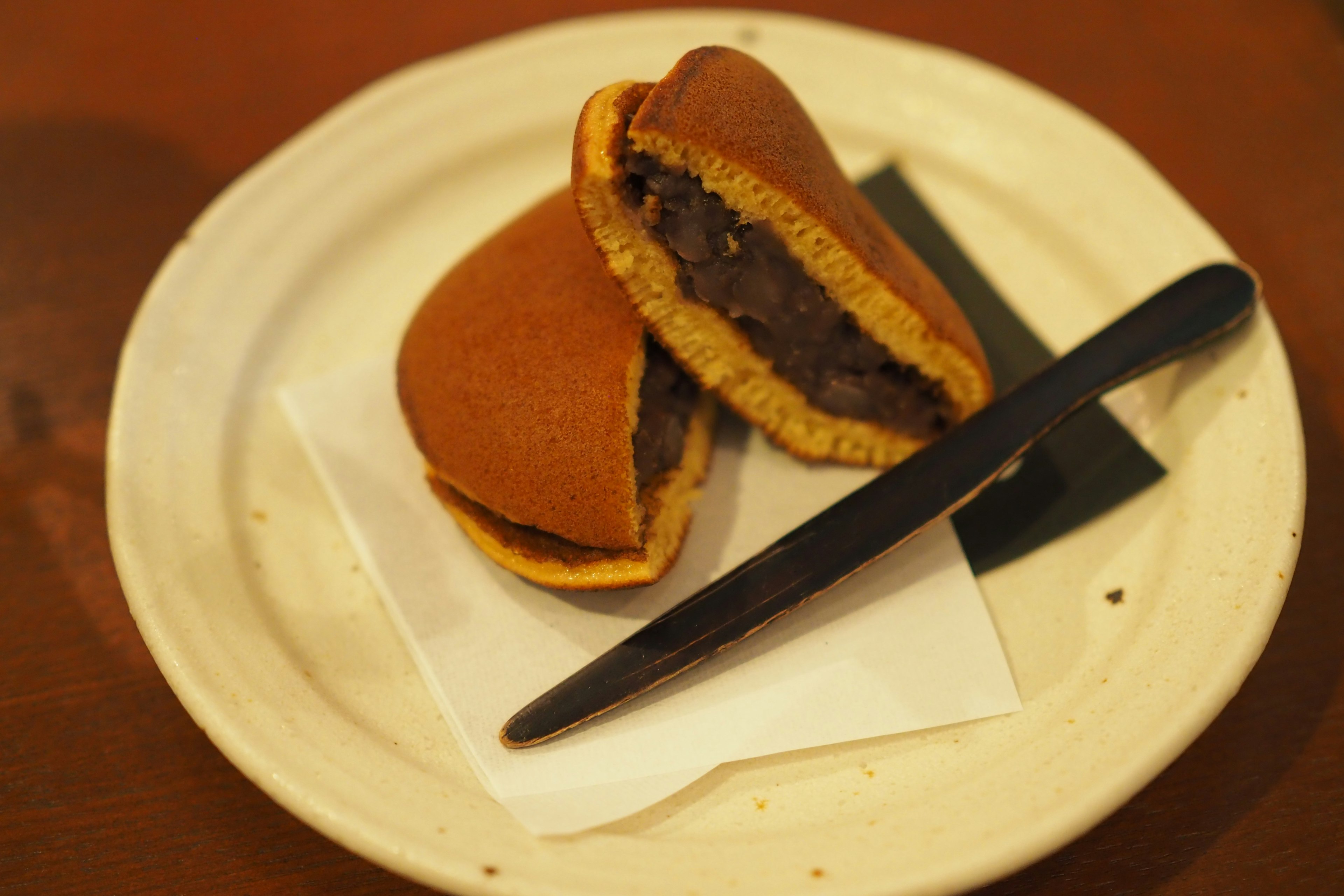 Sebuah piring dengan dua setengah dorayaki yang diisi pasta kacang merah manis dan pisau hitam