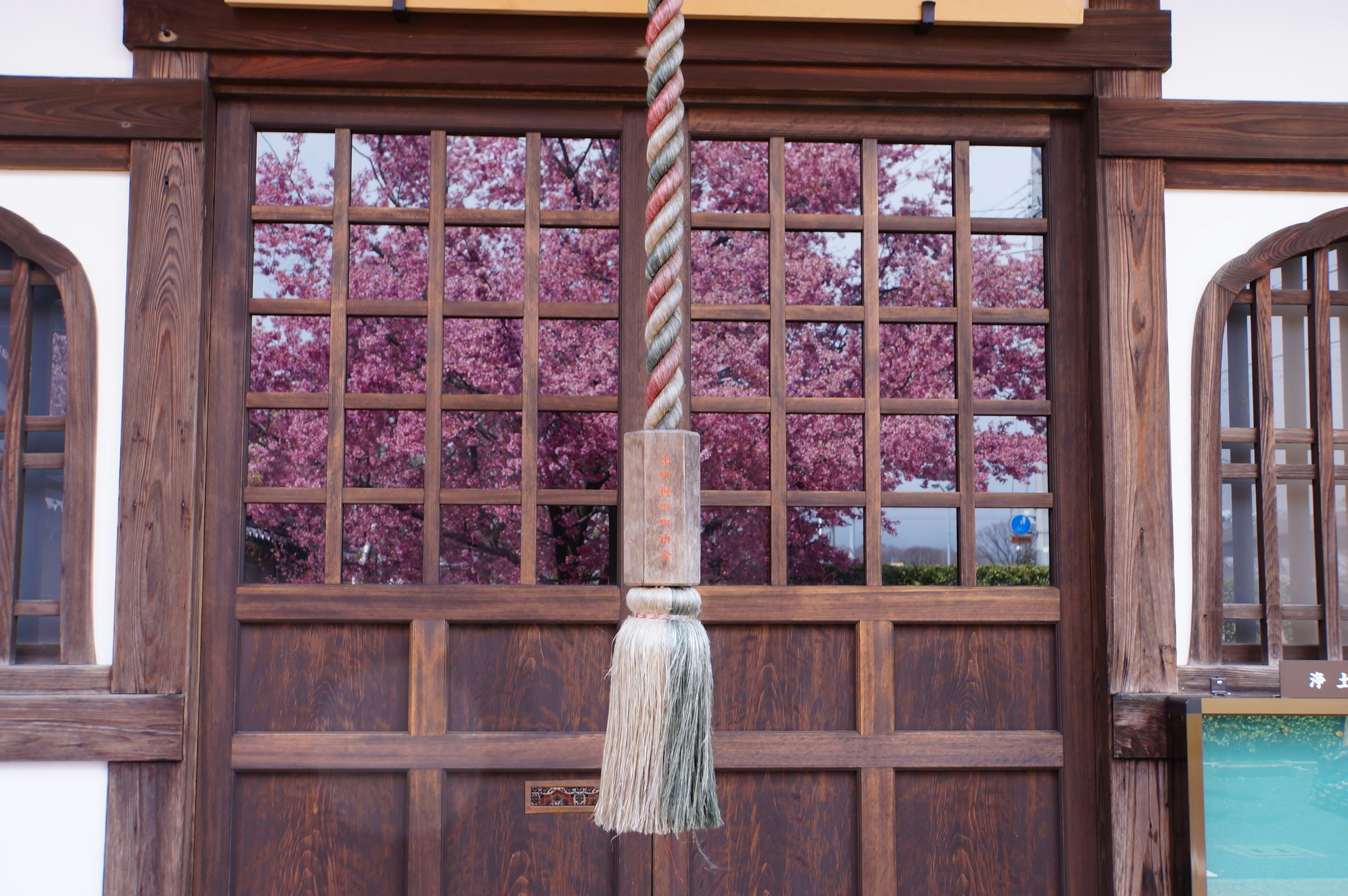 Holztür mit dekorativem Seil und Kirschblüten, die durch die Fenster sichtbar sind