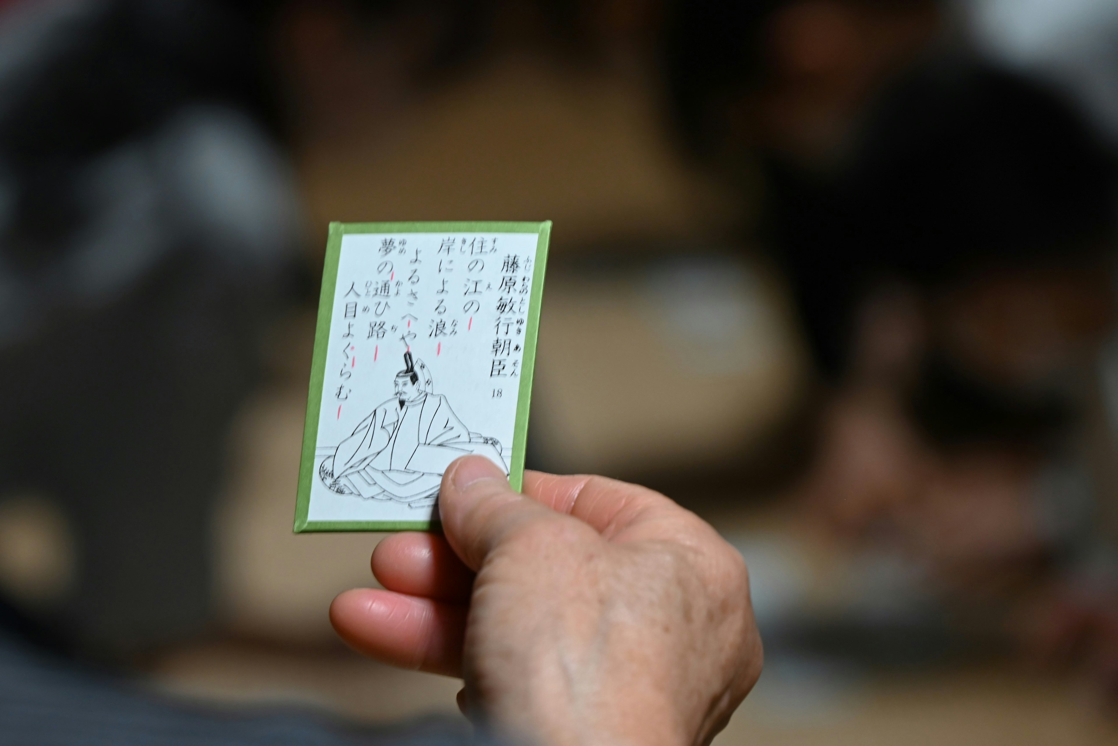 A hand holding a green card featuring a traditional Japanese figure illustration