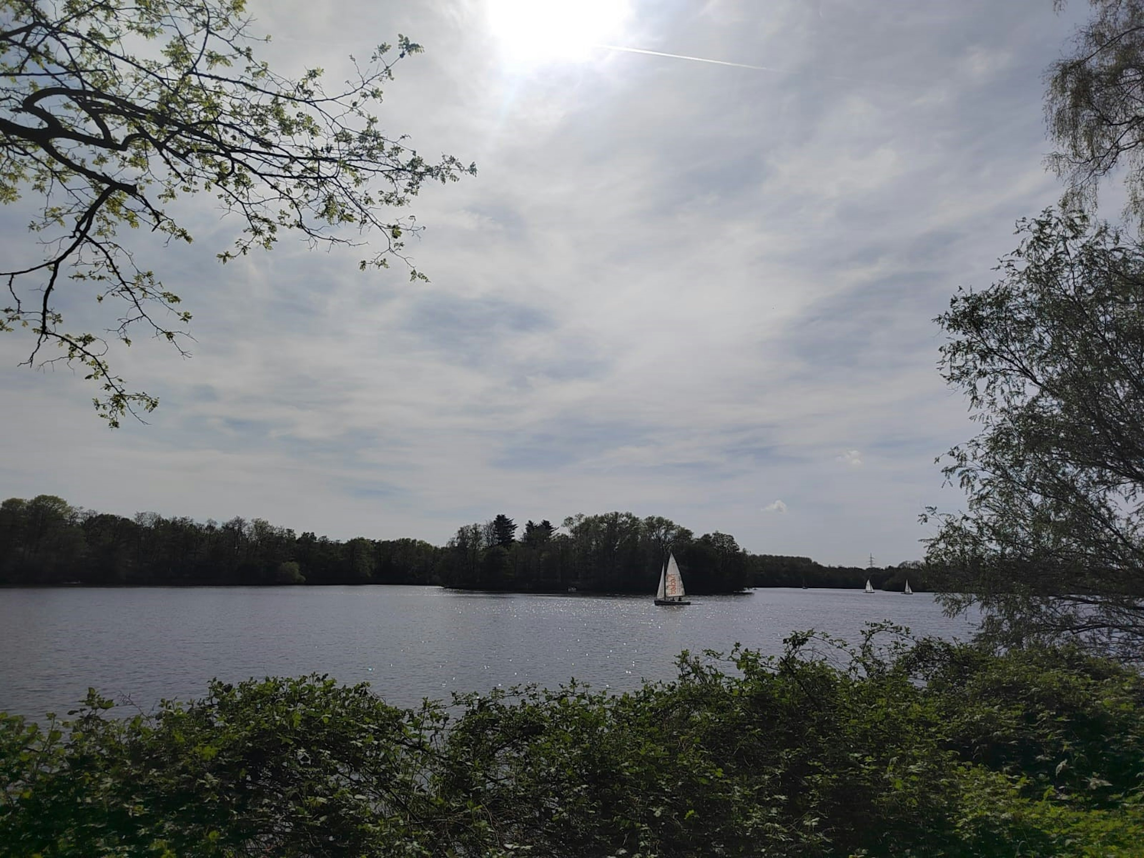 Un lago tranquillo con una vela bianca e cielo nuvoloso