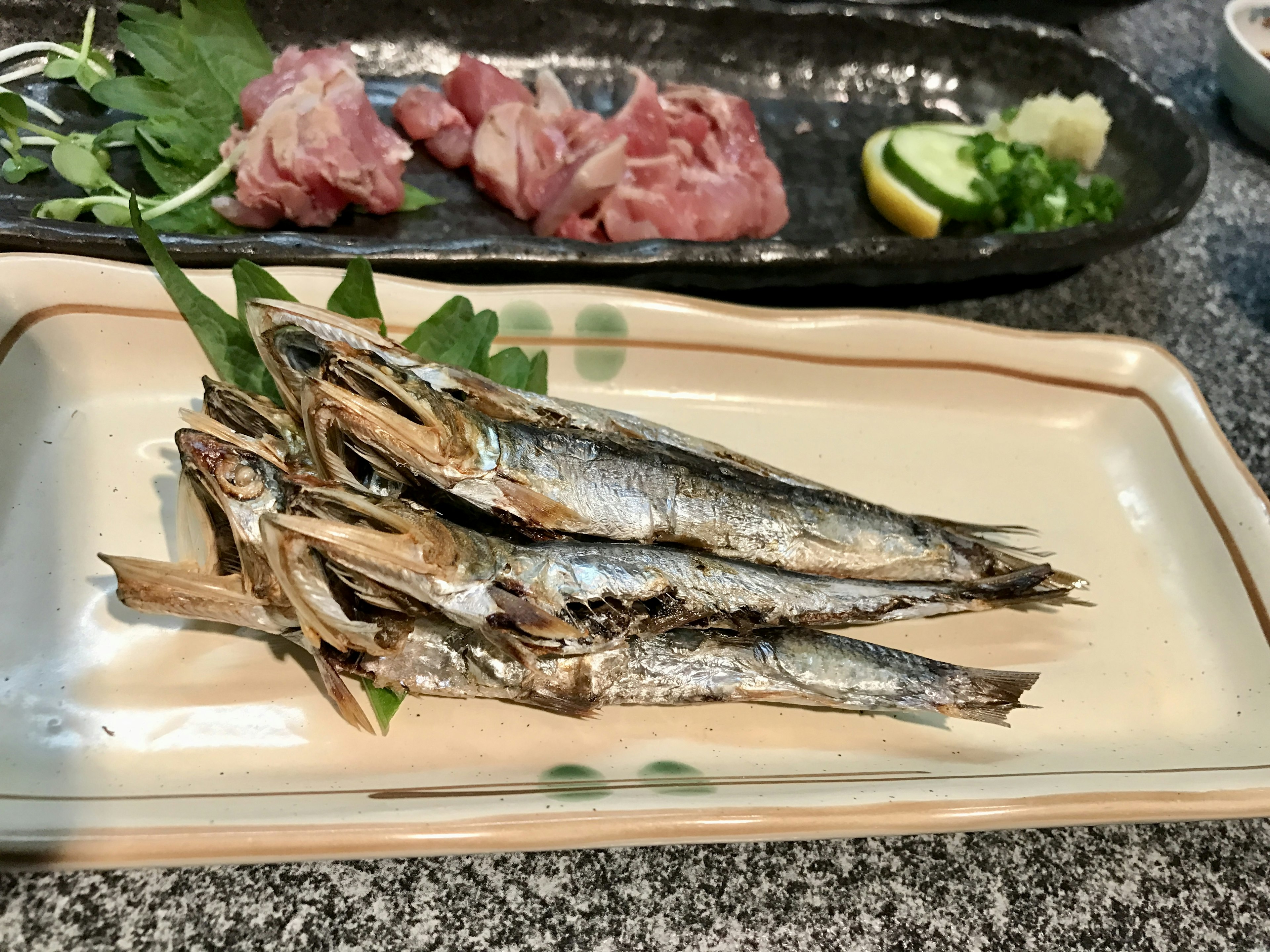 Grilled fish on a plate with raw meat and lemon slices in the background