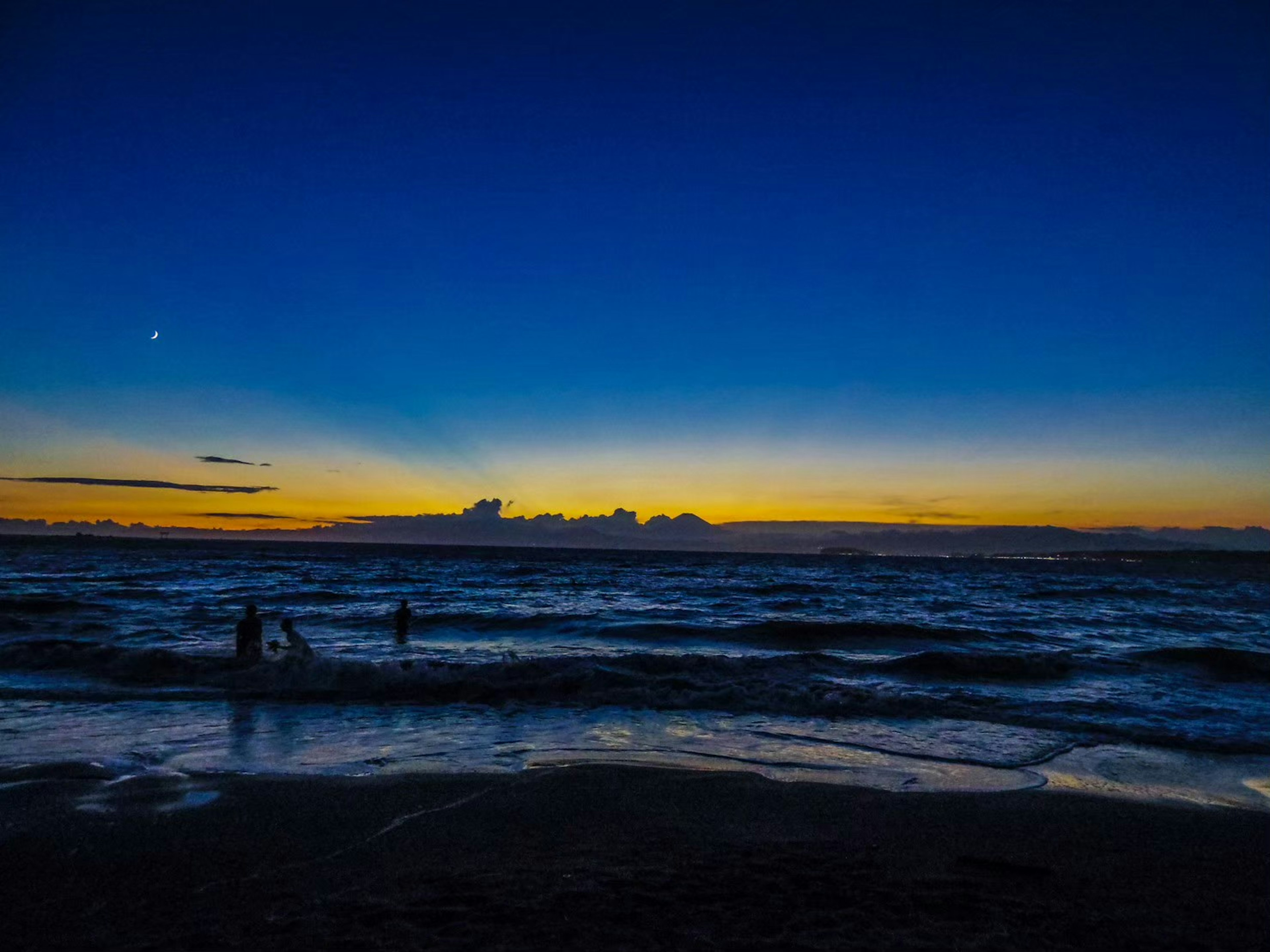 Pemandangan laut yang indah saat matahari terbenam dengan orang-orang di dalam air