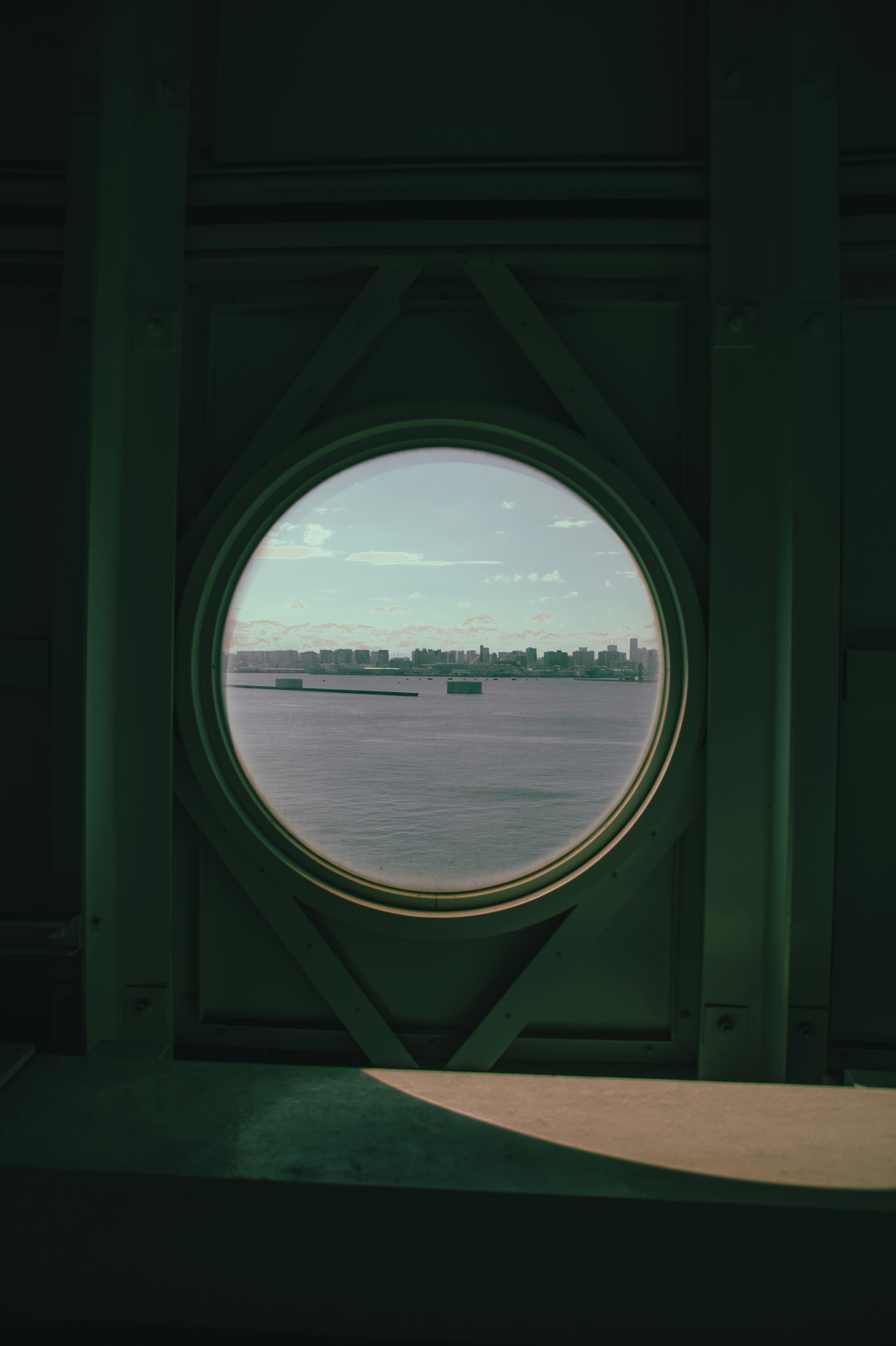 Blick durch ein rundes Fenster auf ruhiges Wasser und eine entfernte Landschaft