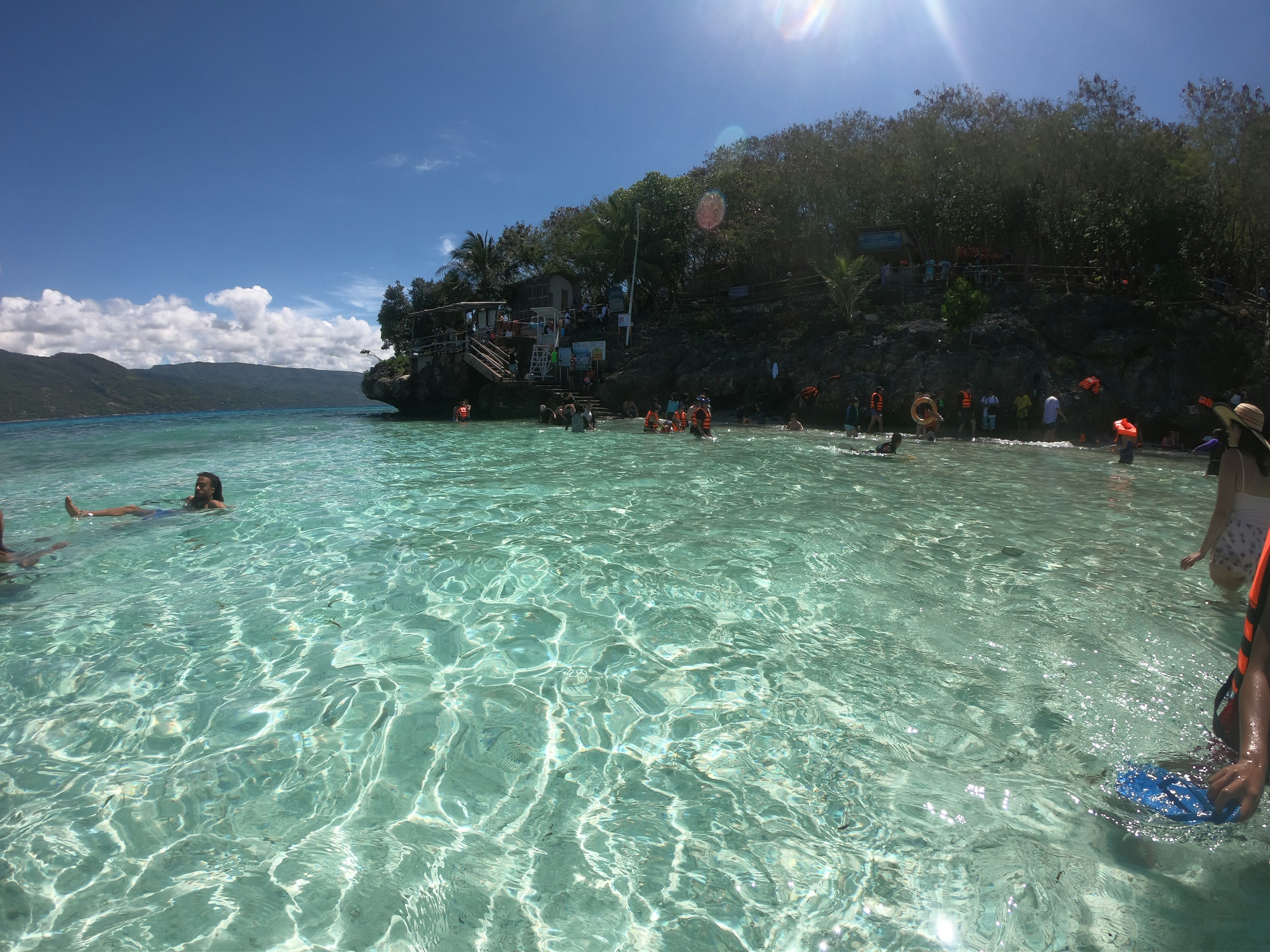 Pemandangan pantai dengan air jernih dan orang-orang menikmati matahari