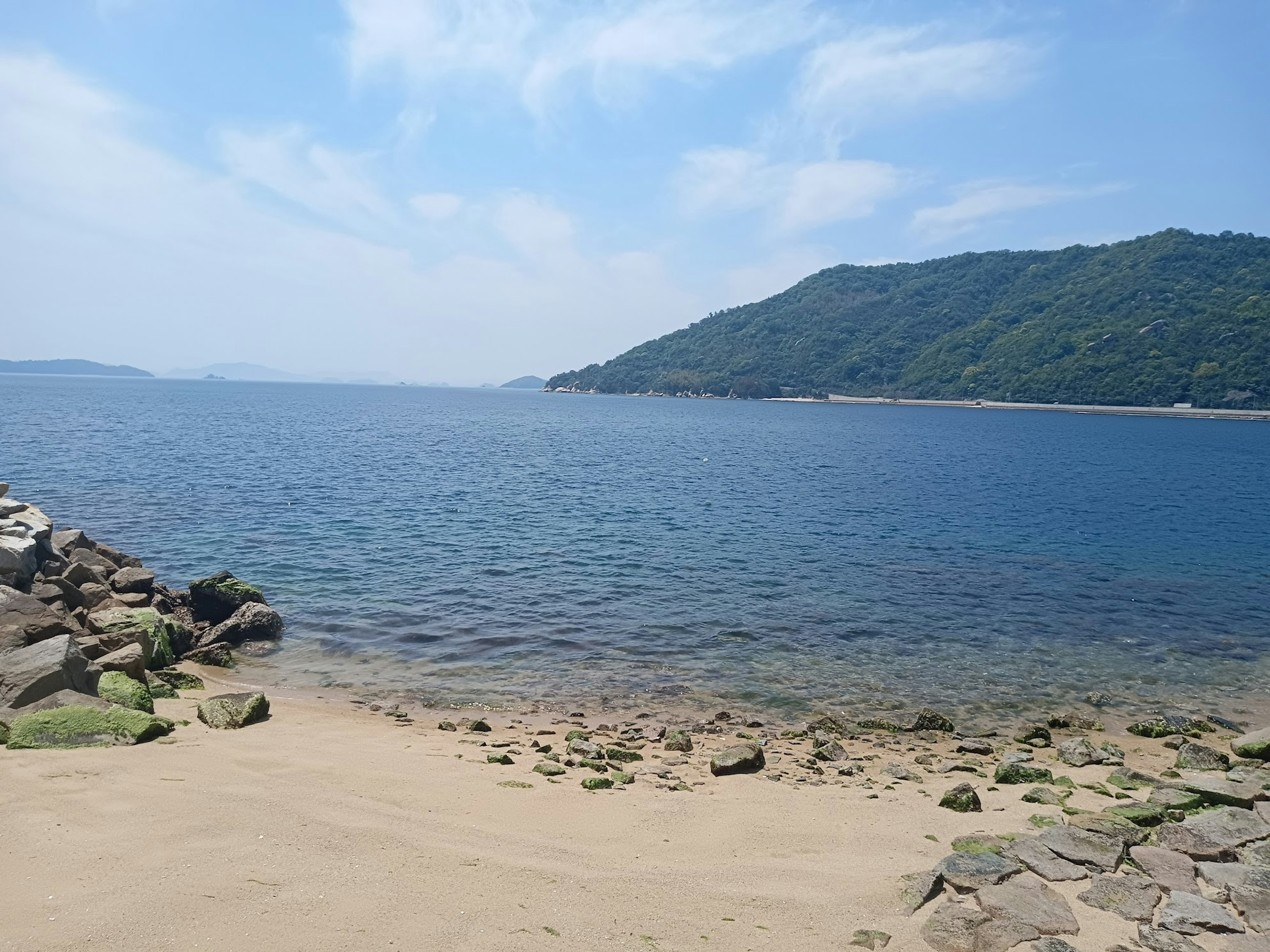 Pemandangan laut biru dan pantai berpasir dengan bukit hijau di latar belakang