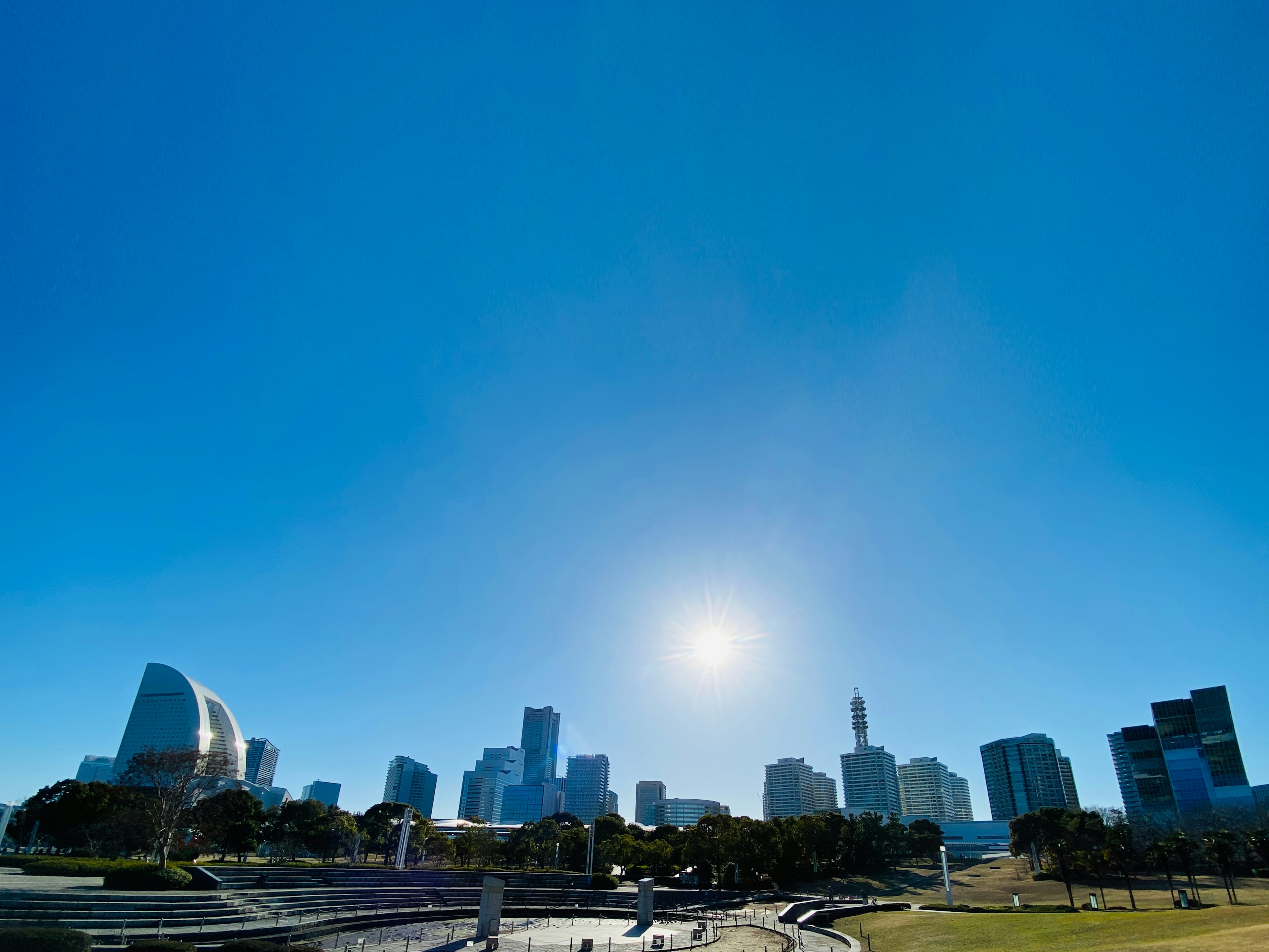 City skyline with tall buildings under a clear blue sky bright sun in background