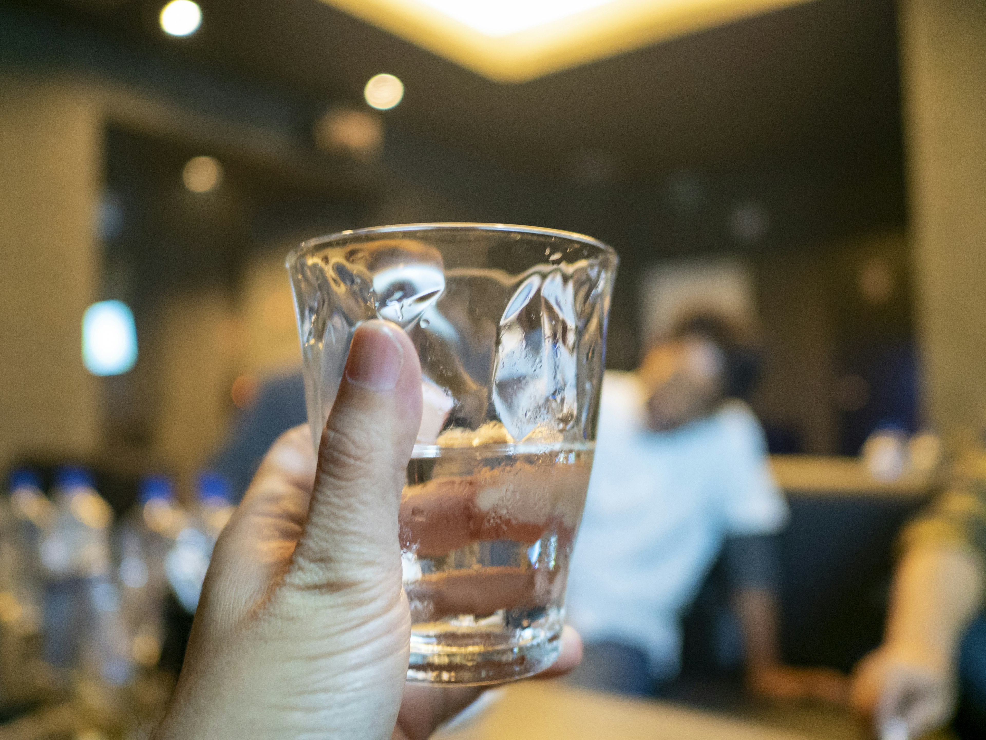 Person holding a glass with ice and water with blurred people in the background