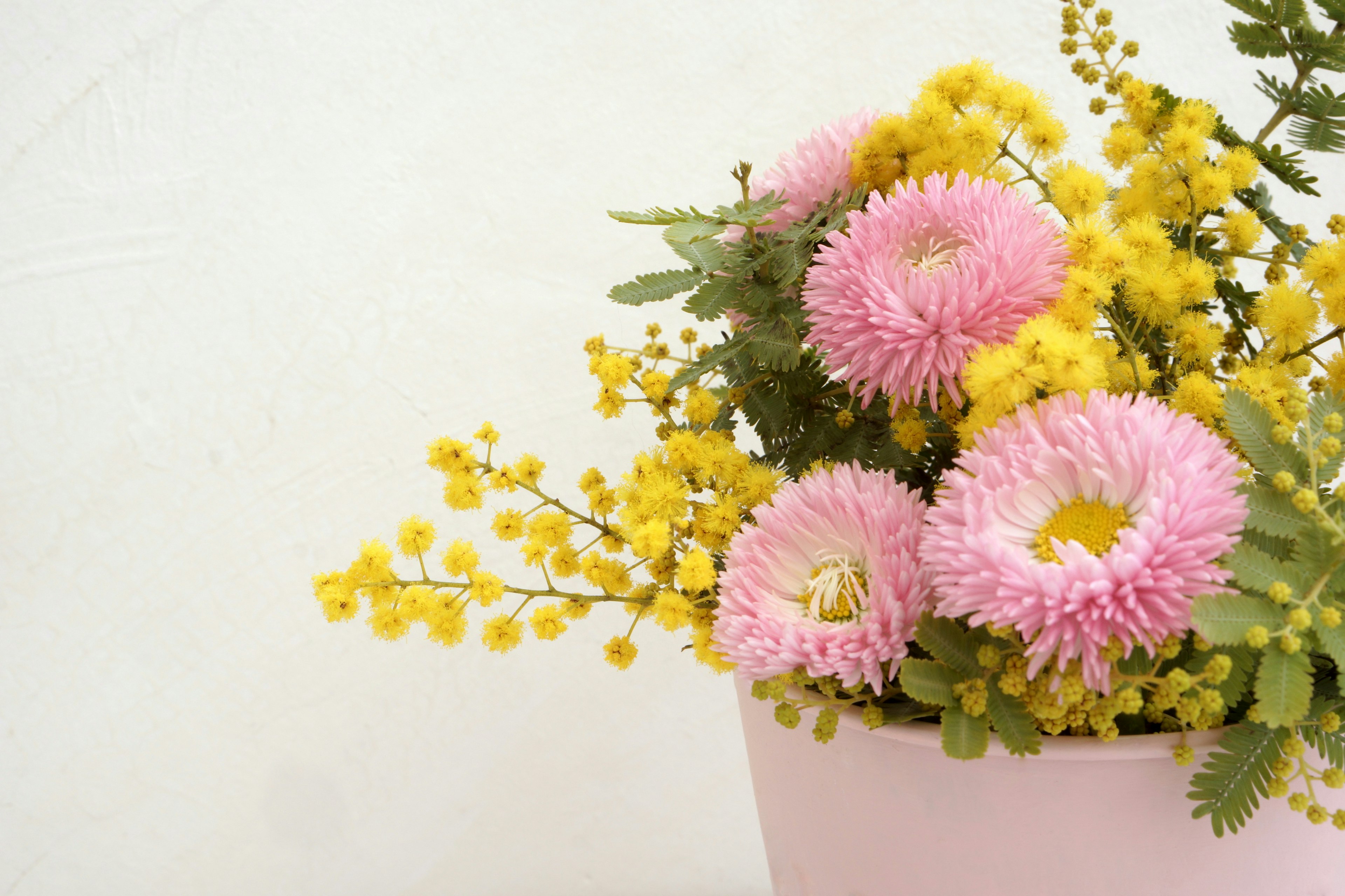 Strauß aus rosa und gelben Blumen in einem rosa Topf vor weißem Hintergrund