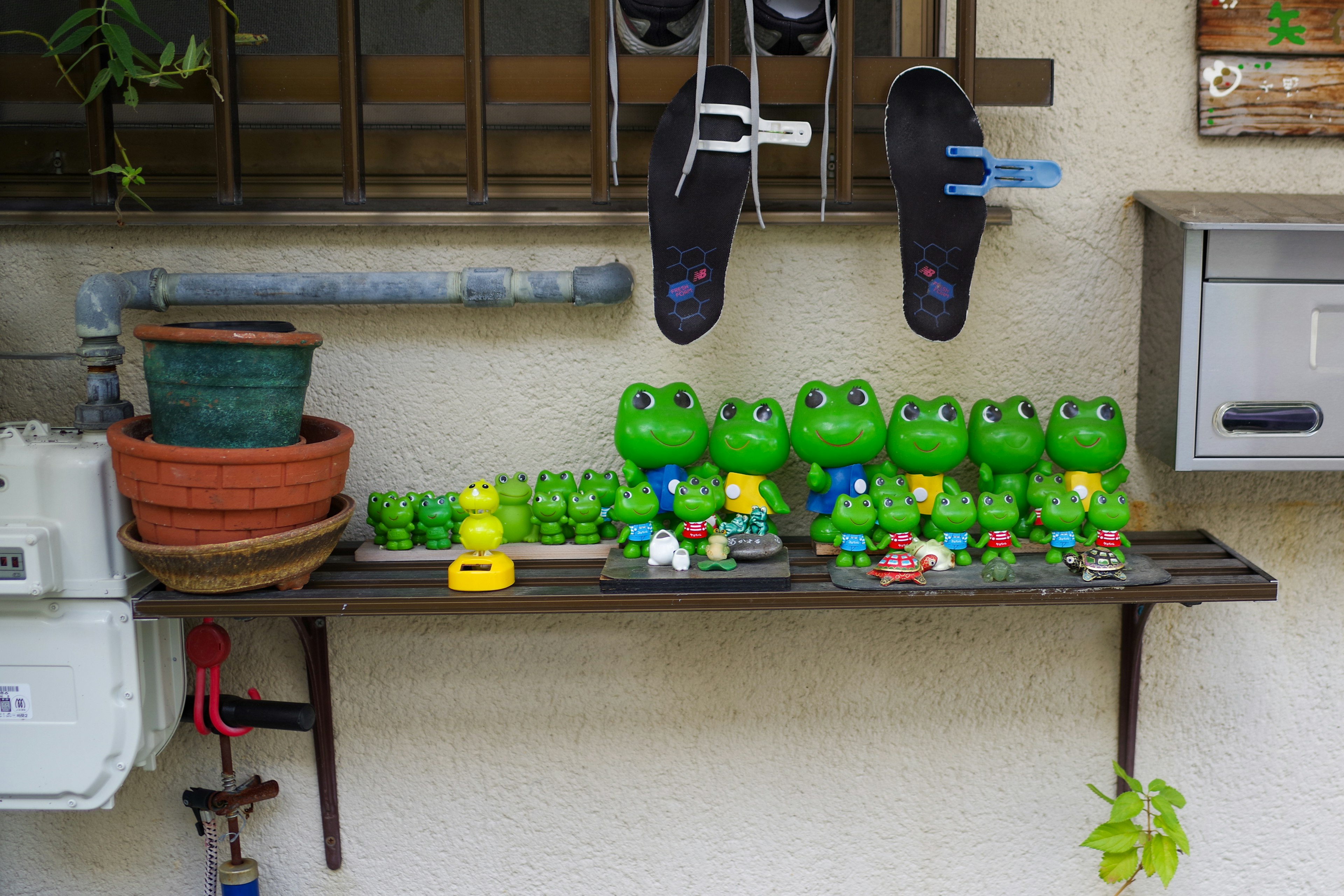 Une étagère avec des figurines de grenouilles vertes et des pots de fleurs à l'extérieur d'un bâtiment