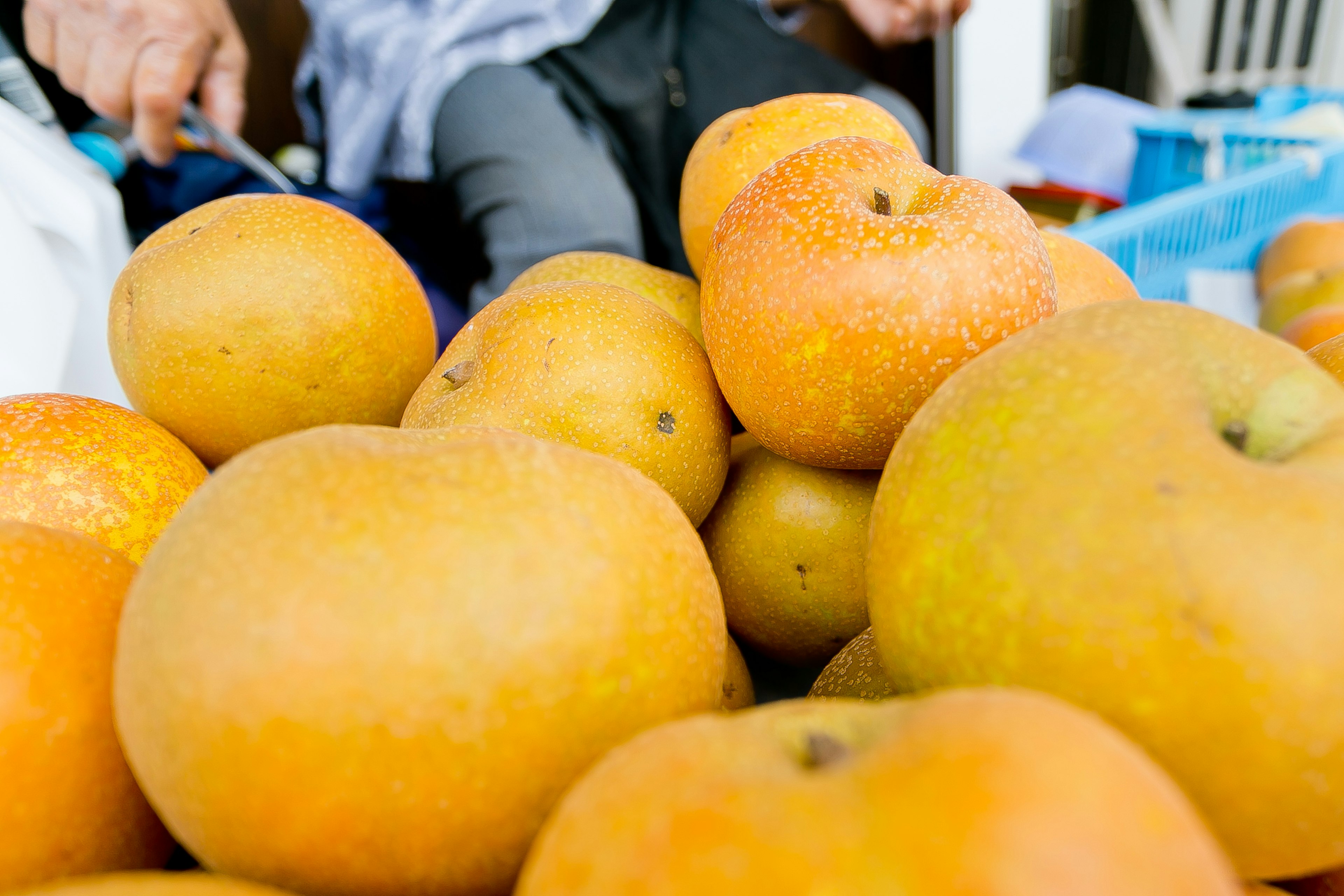 A pile of orange fruits with a person's hand in the background