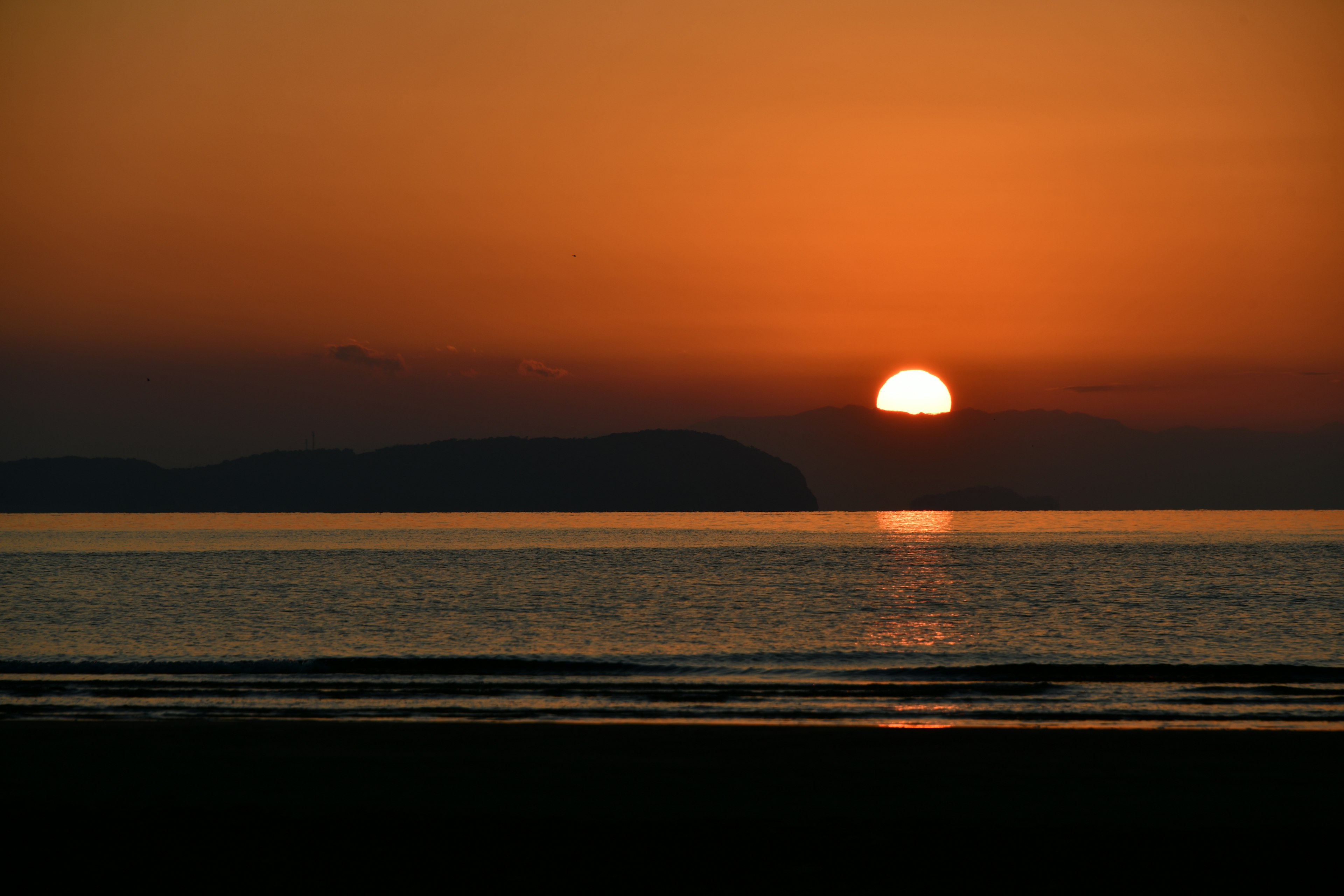 Sonnenuntergang über dem Ozean mit Silhouette von fernen Hügeln