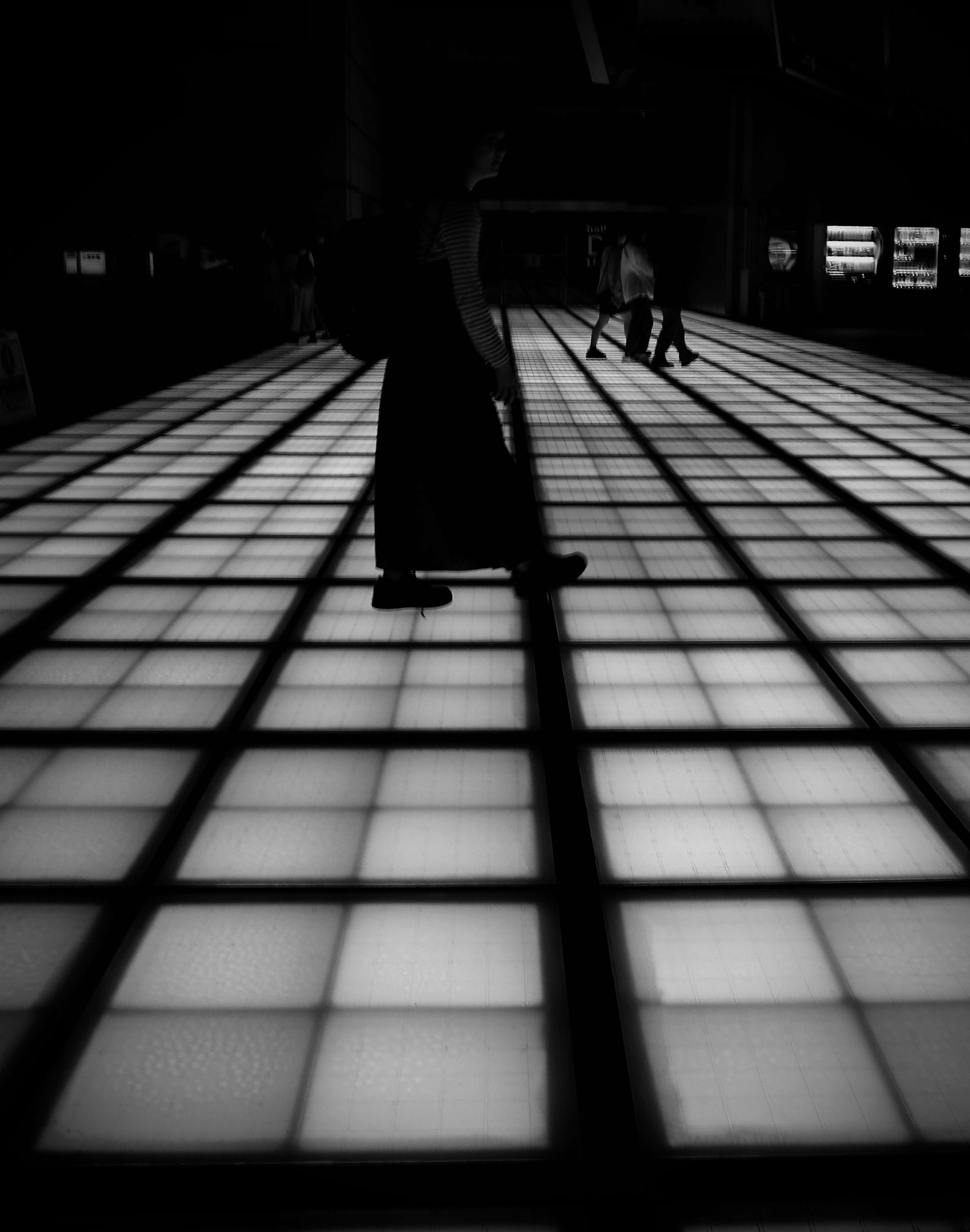 Silhouettes de personnes marchant sur un sol lumineux en noir et blanc