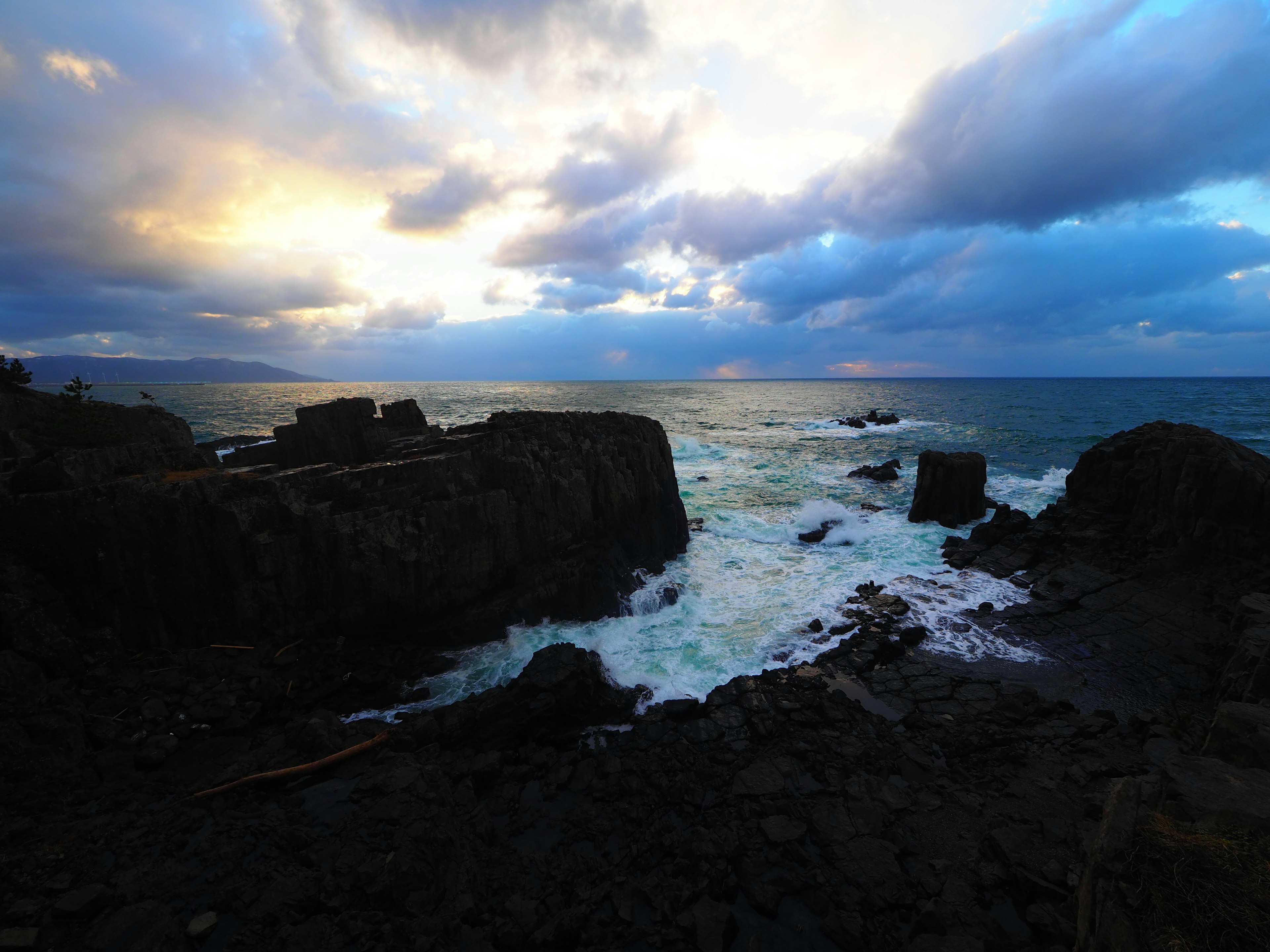 Paesaggio costiero con rocce e onde, cielo blu e nuvole