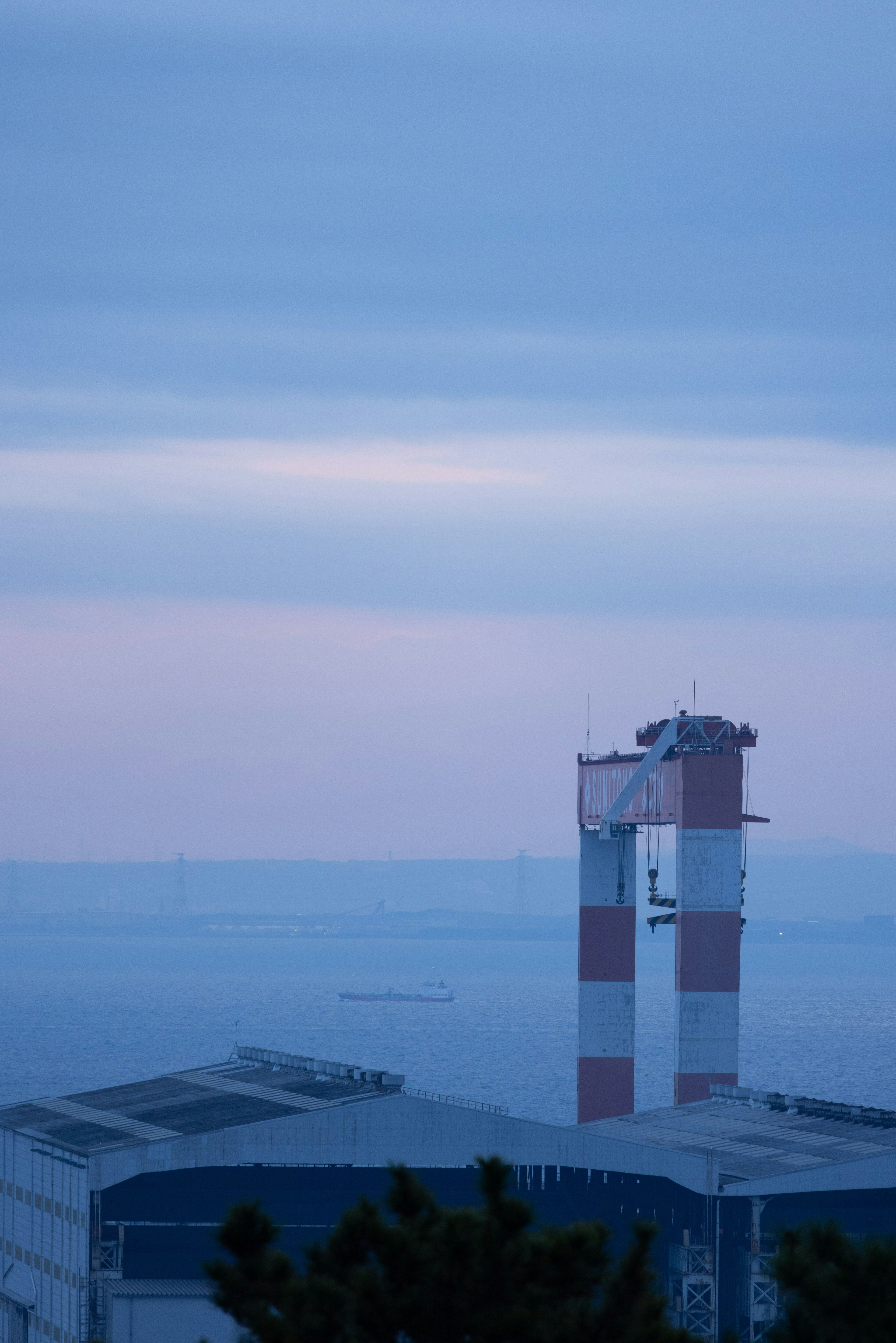 Fabriklandschaft mit einem rot-weißen Schornstein vor blauem Himmel und Meer