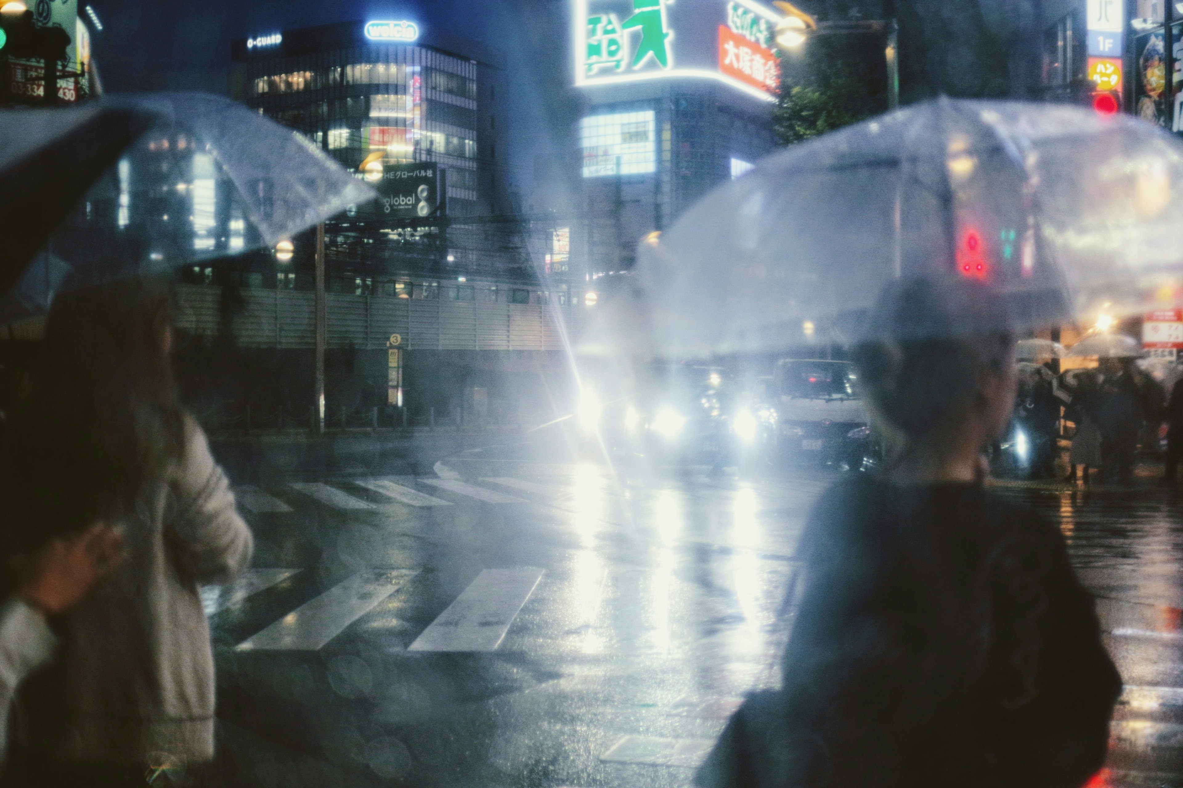 Night scene with people holding umbrellas and city lights in the rain