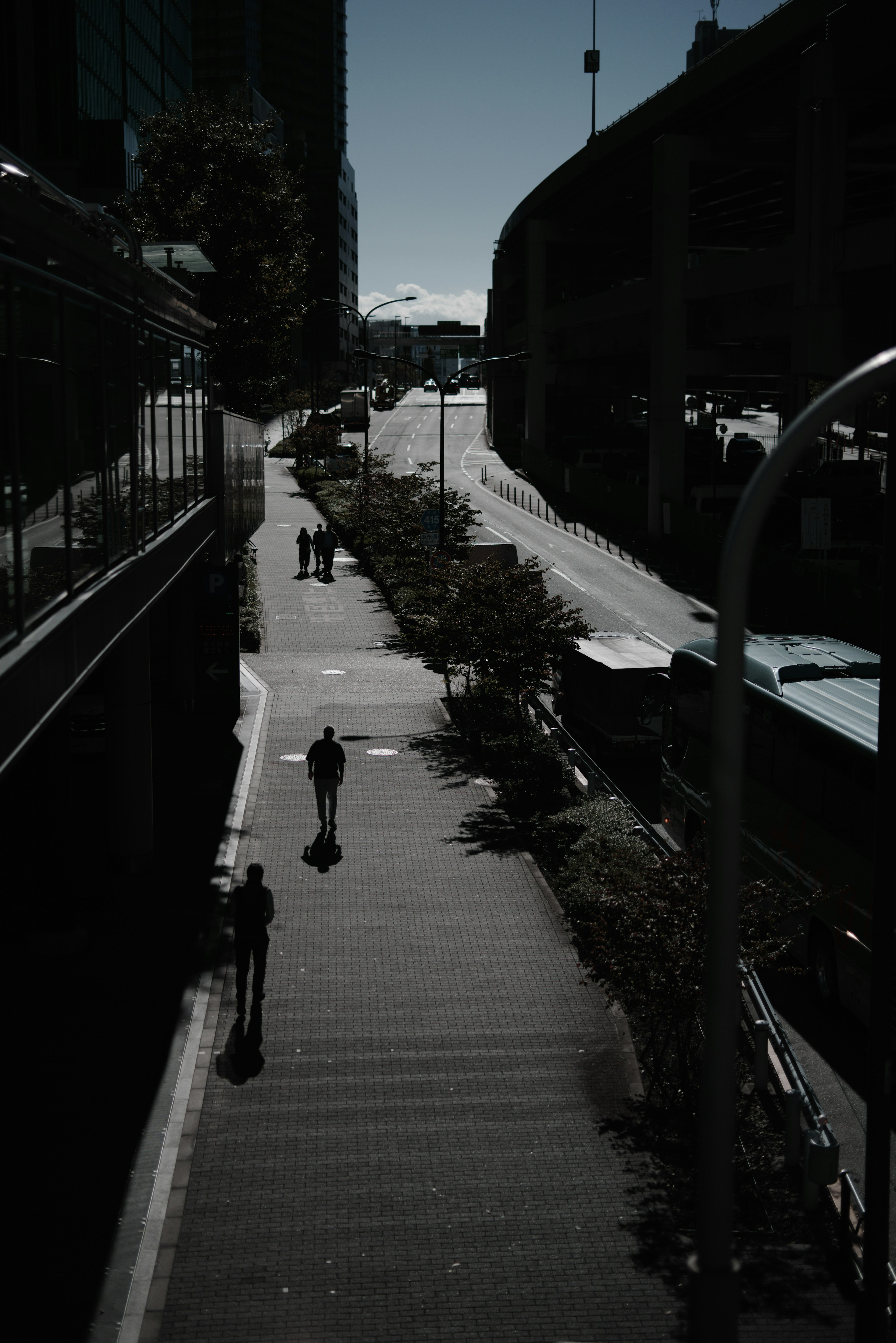 Städtische Szene mit Menschen, die auf einem Gehweg im Schatten gehen