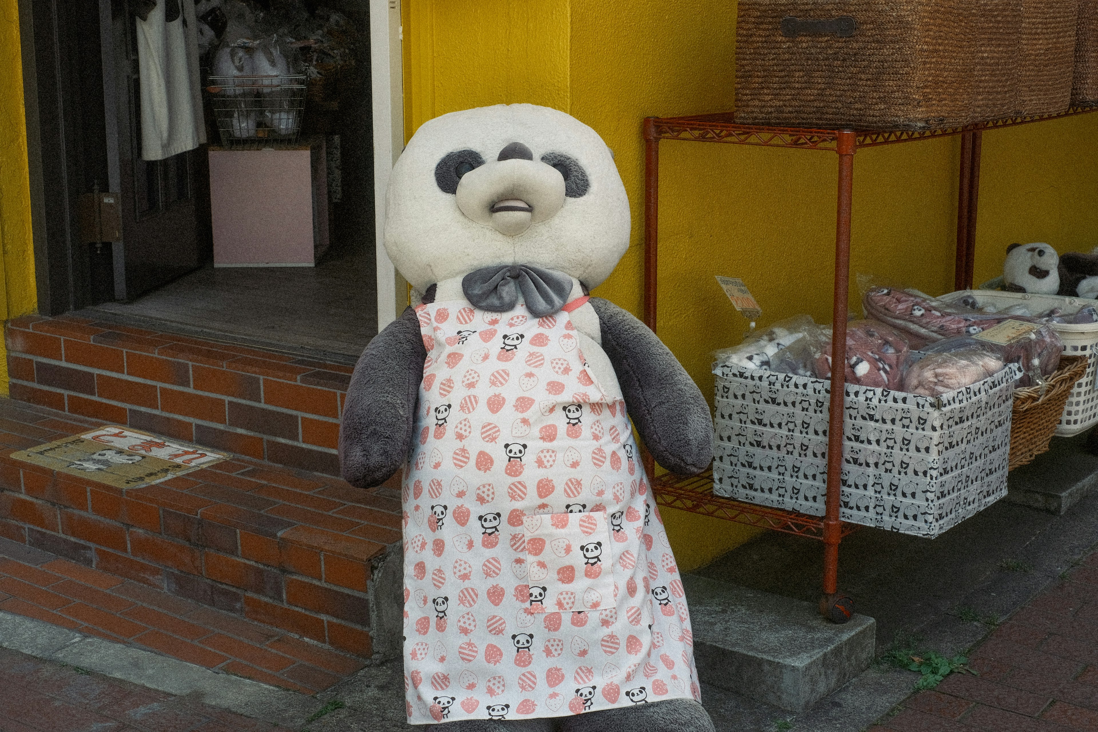 Una mascota panda con un delantal está de pie frente a una tienda