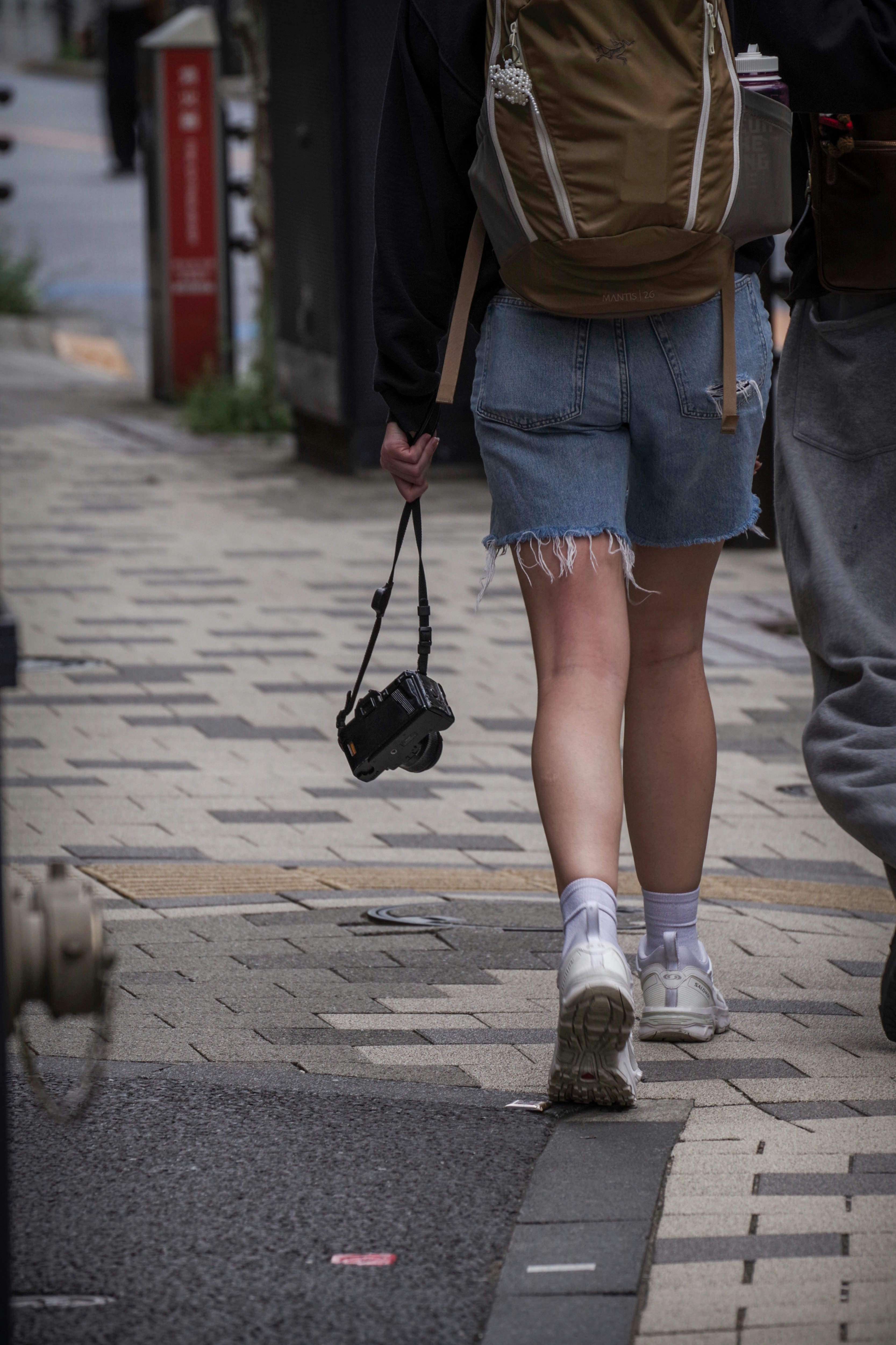 Eine Person in Jeansshorts, die mit einer Kamera in einer städtischen Umgebung geht