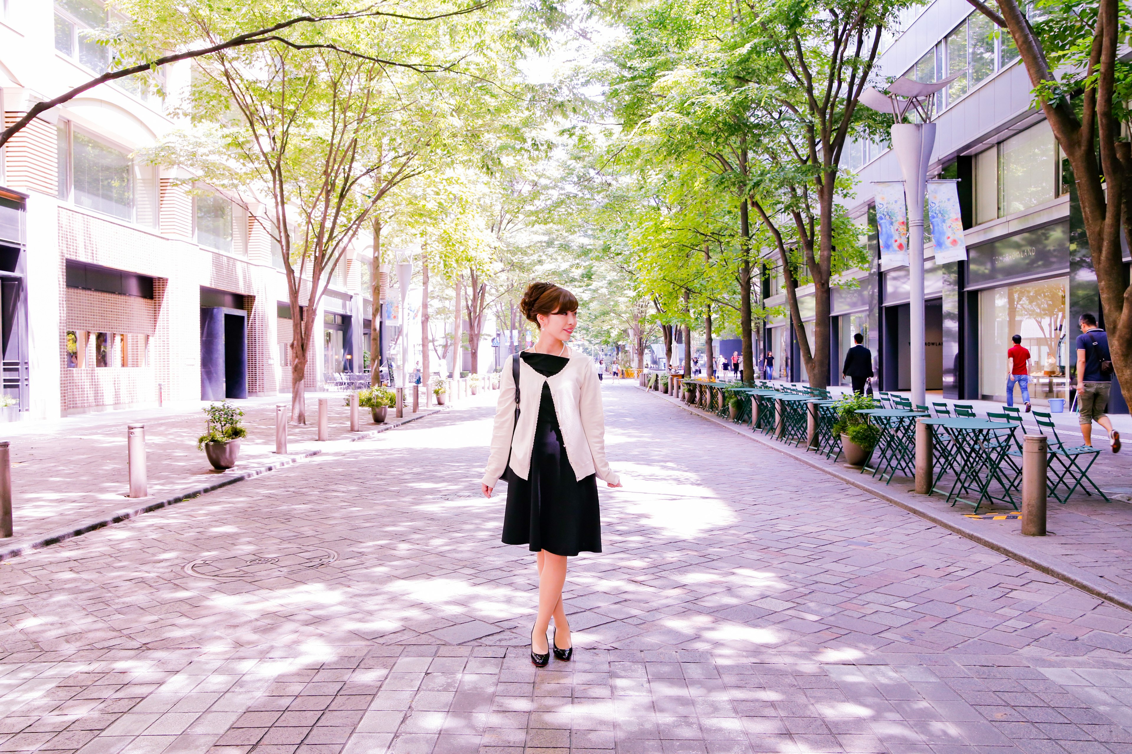 A woman walking on a tree-lined street with shops and greenery