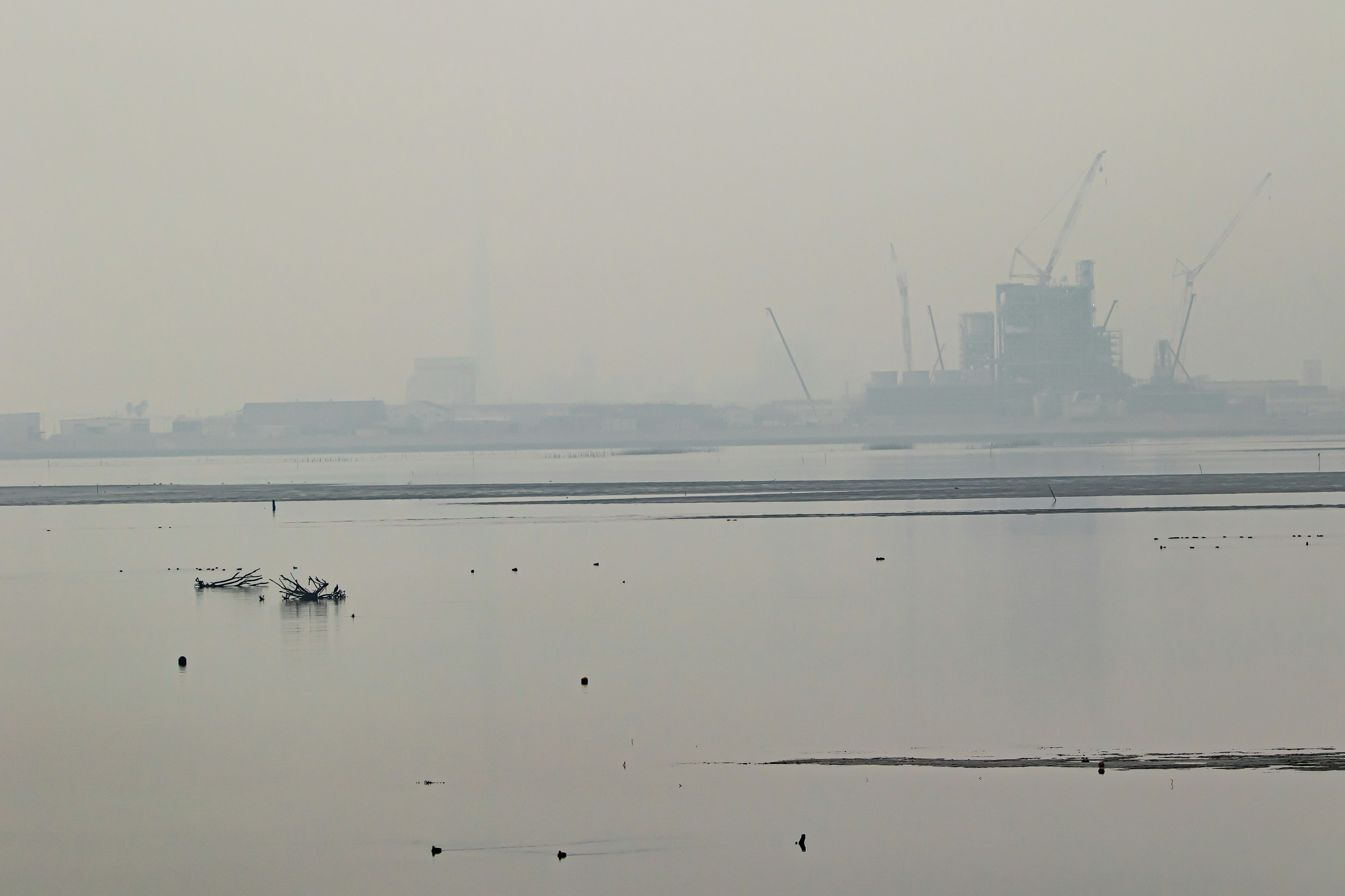 Zona industrial con niebla y pequeño barco en agua tranquila