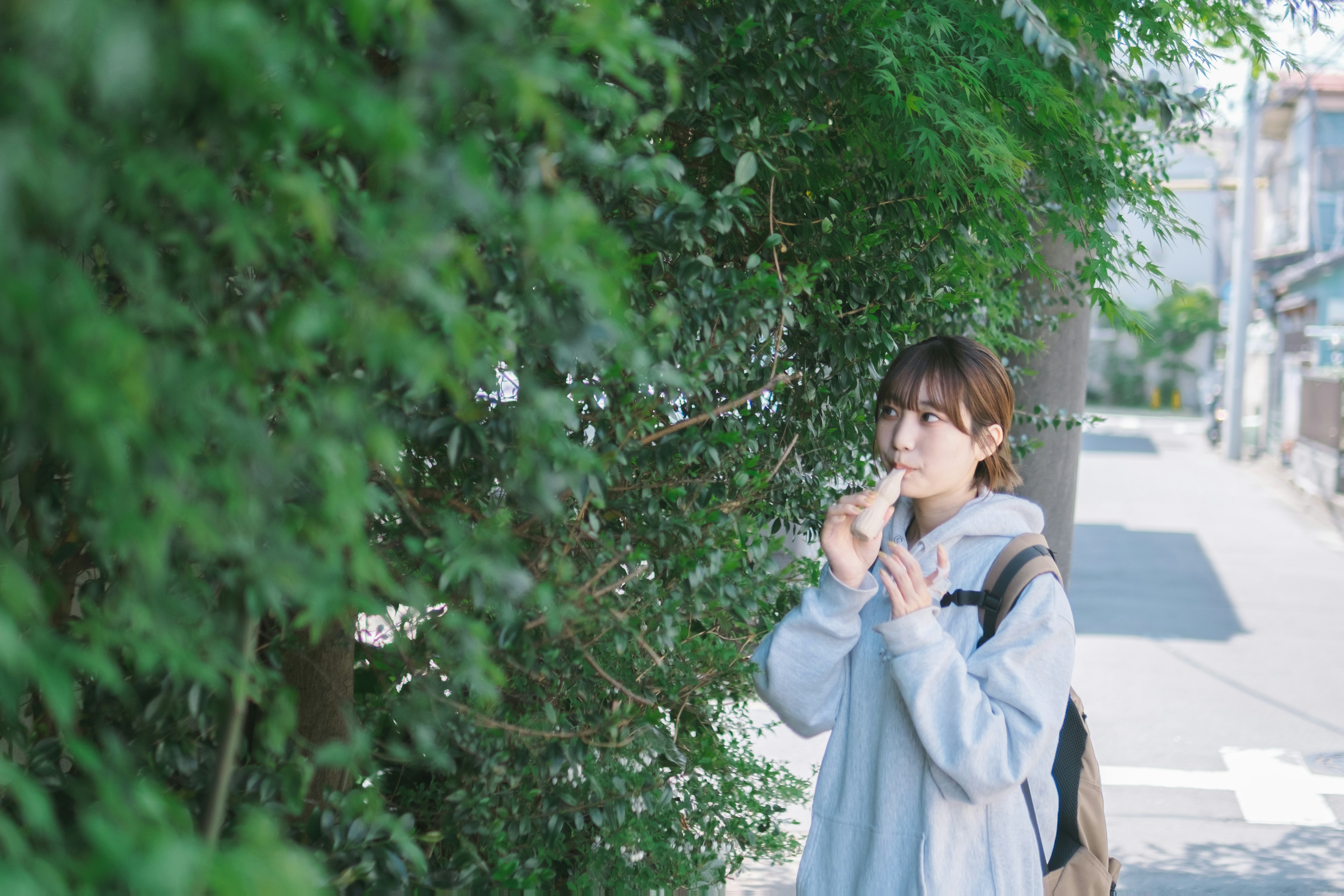 Young woman standing near green bushes enjoying ice cream