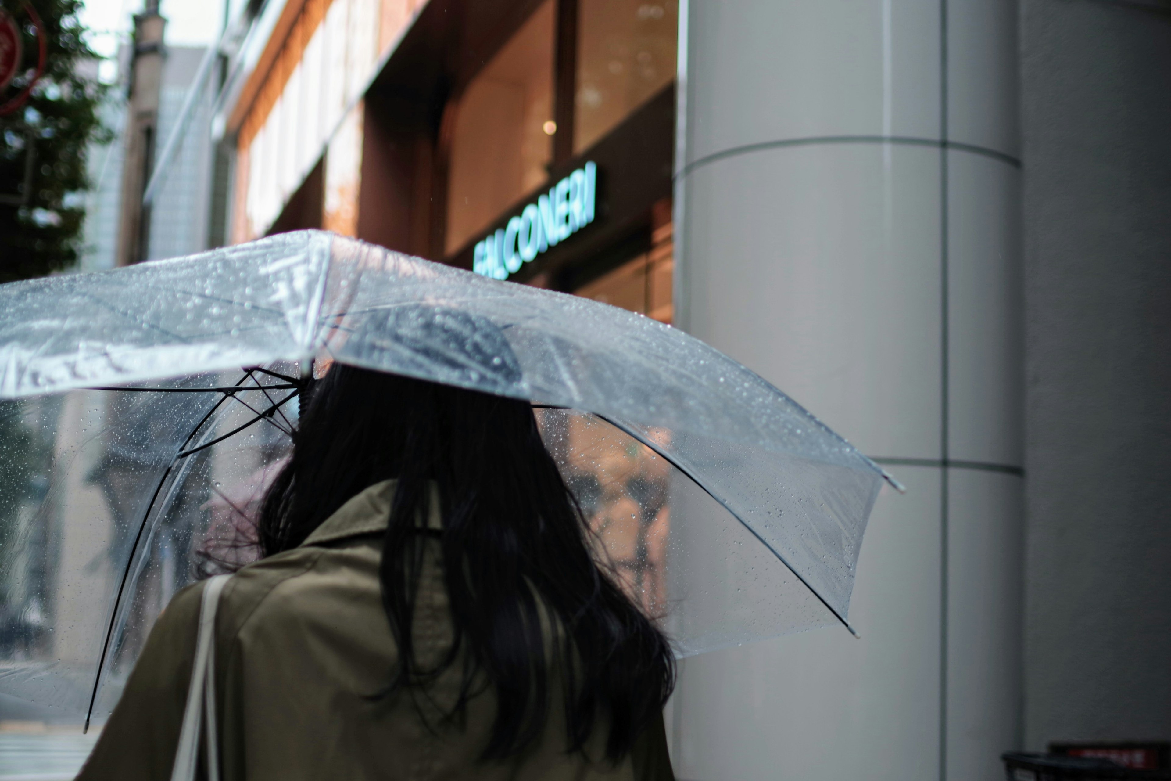 Mujer sosteniendo un paraguas transparente con una vitrina de tienda de ropa al fondo