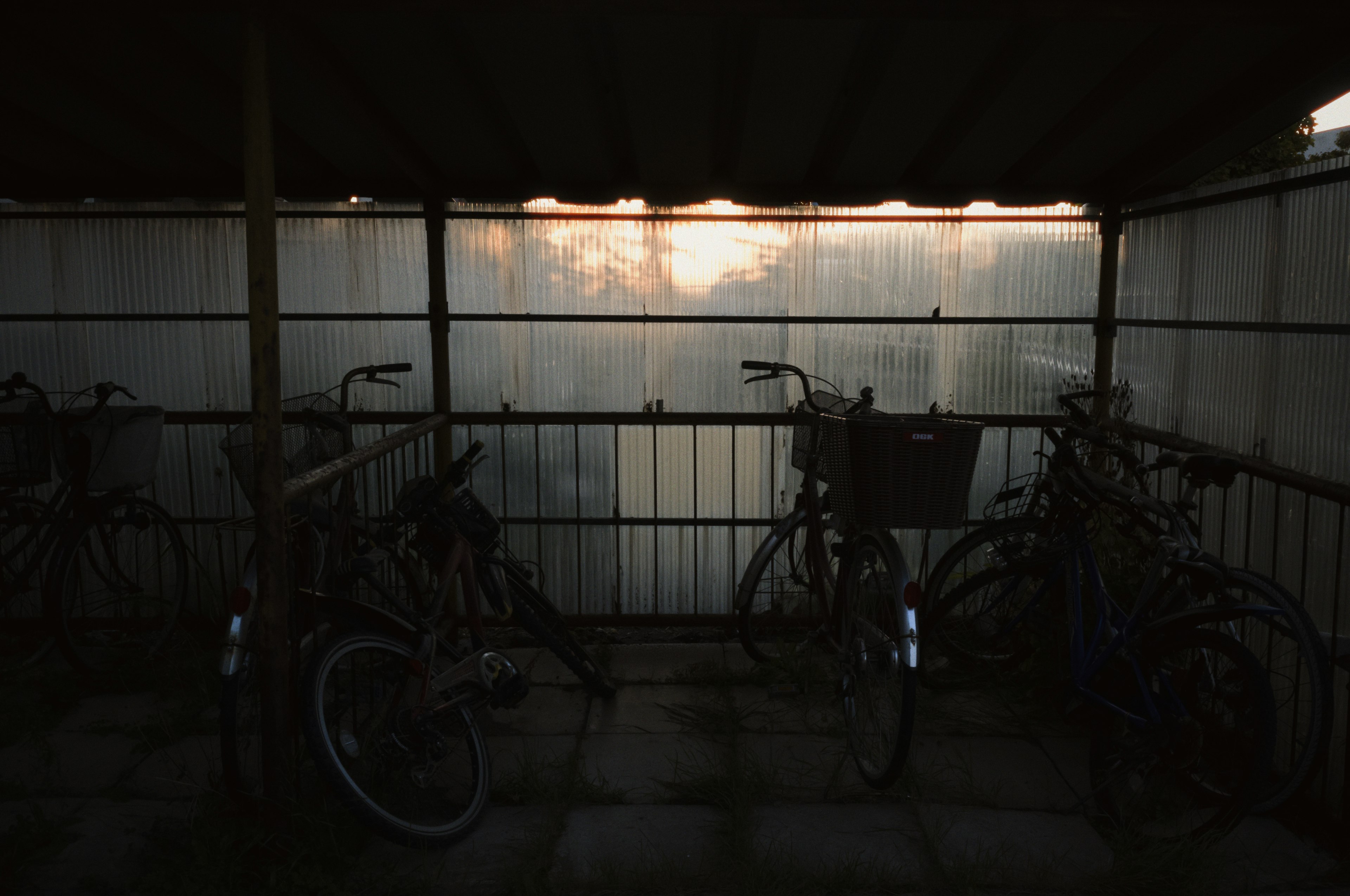 Innenraum eines überdachten Fahrradparkplatzes mit Fahrrädern, schwach beleuchtet durch das Abendlicht