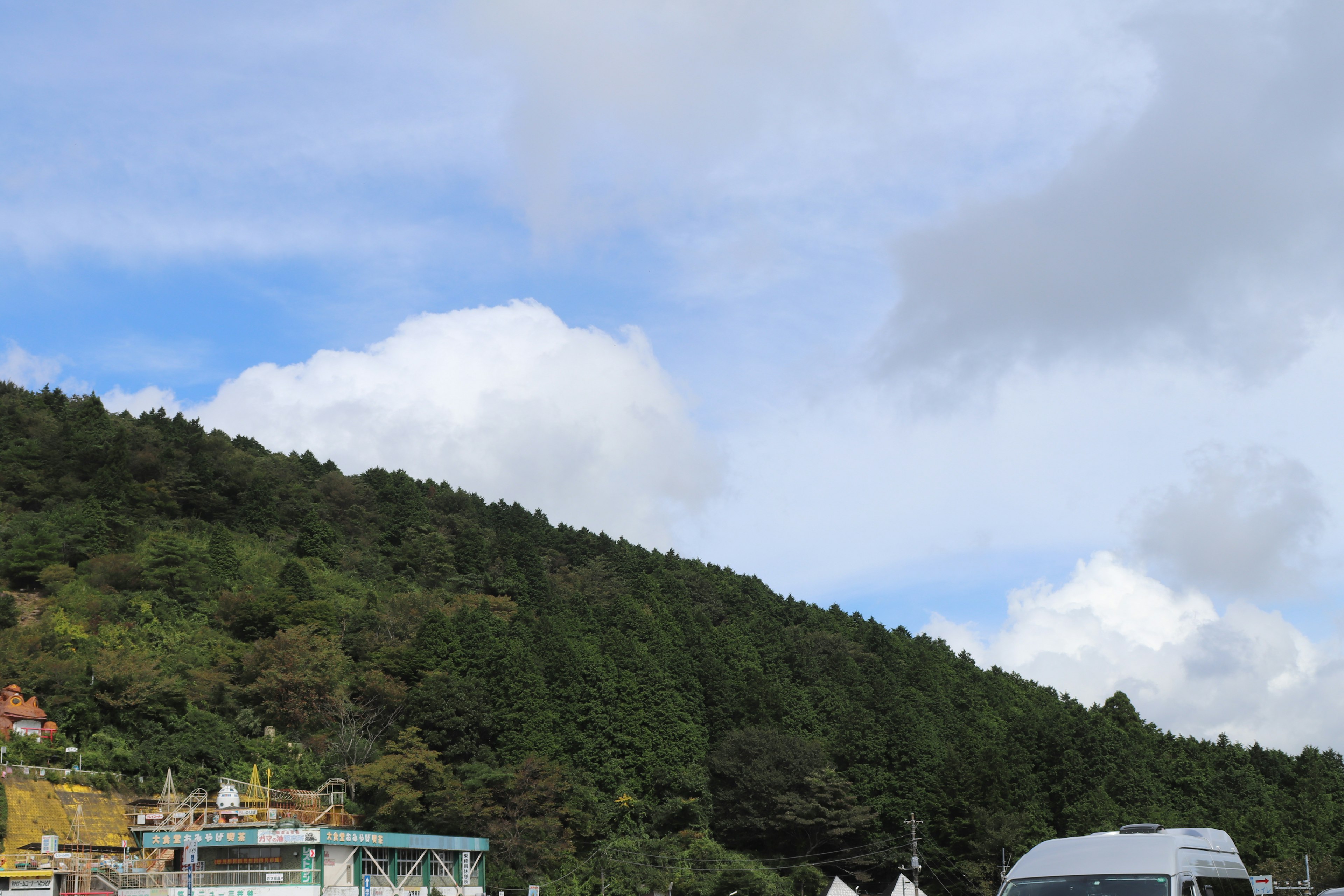 Un paysage avec des collines vertes et un ciel bleu avec des bâtiments et un camping-car