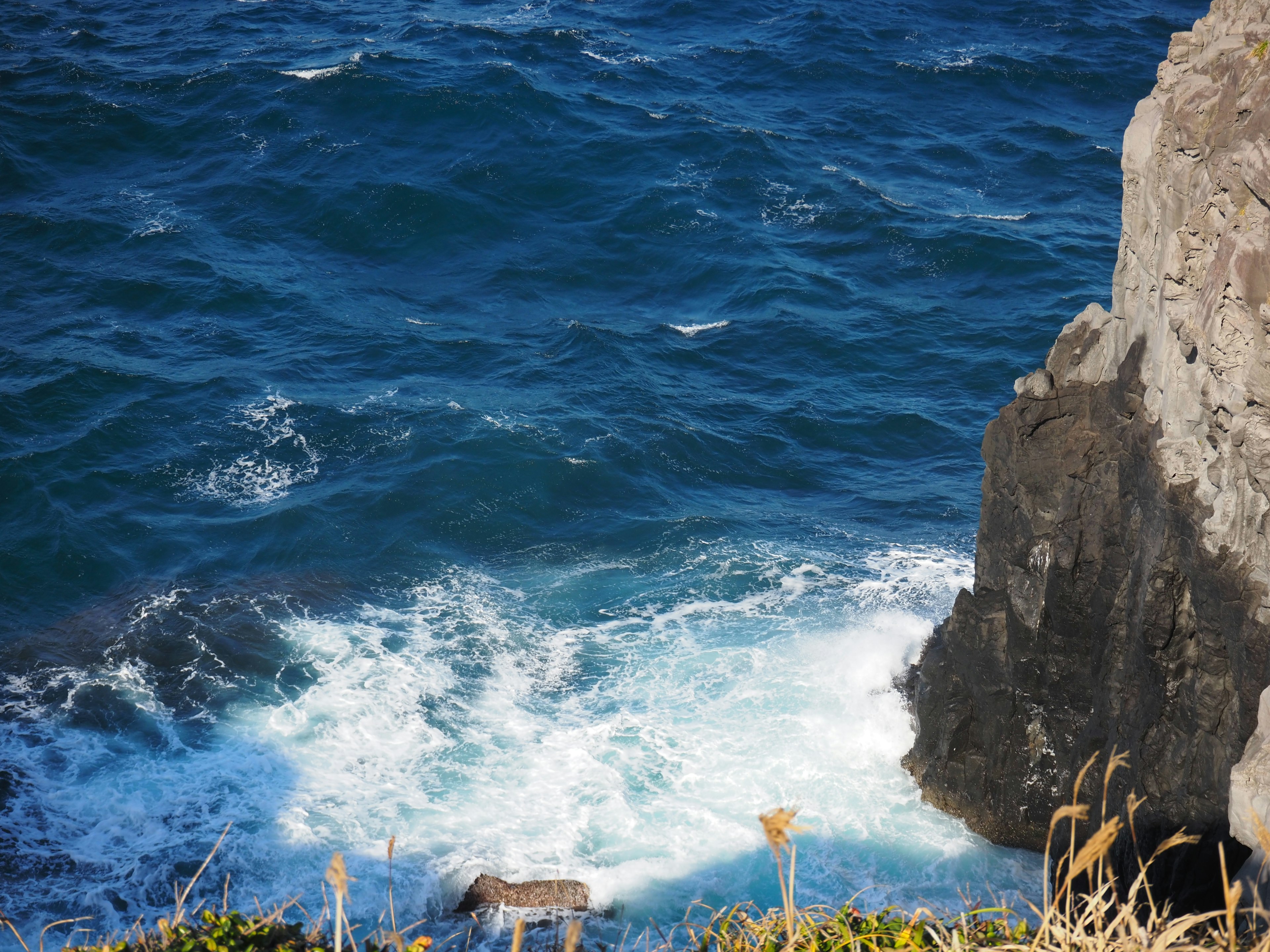 Vista escénica de las olas azules del océano rompiendo contra un acantilado rocoso