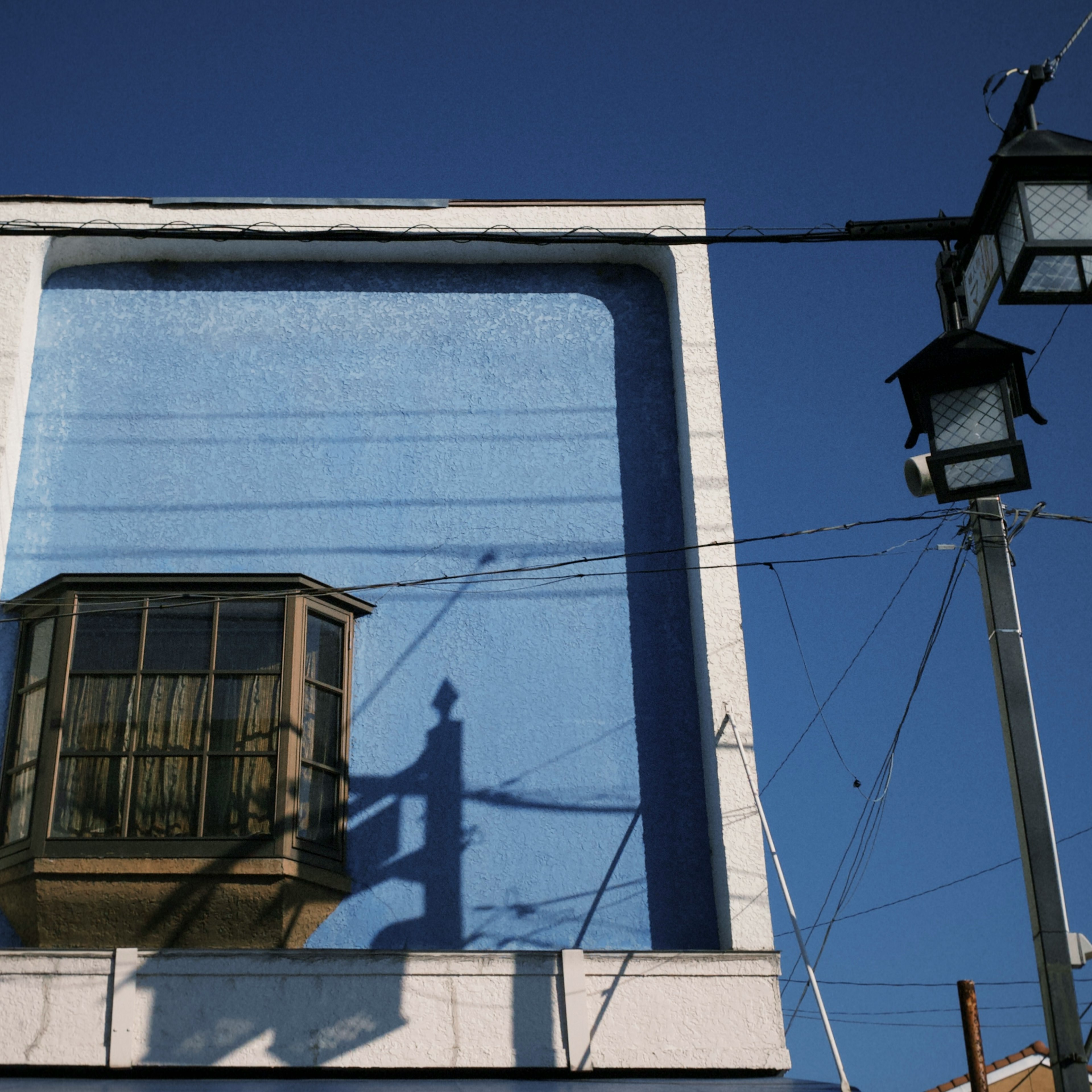 Partie d'un bâtiment avec un mur bleu et l'ombre d'une fenêtre