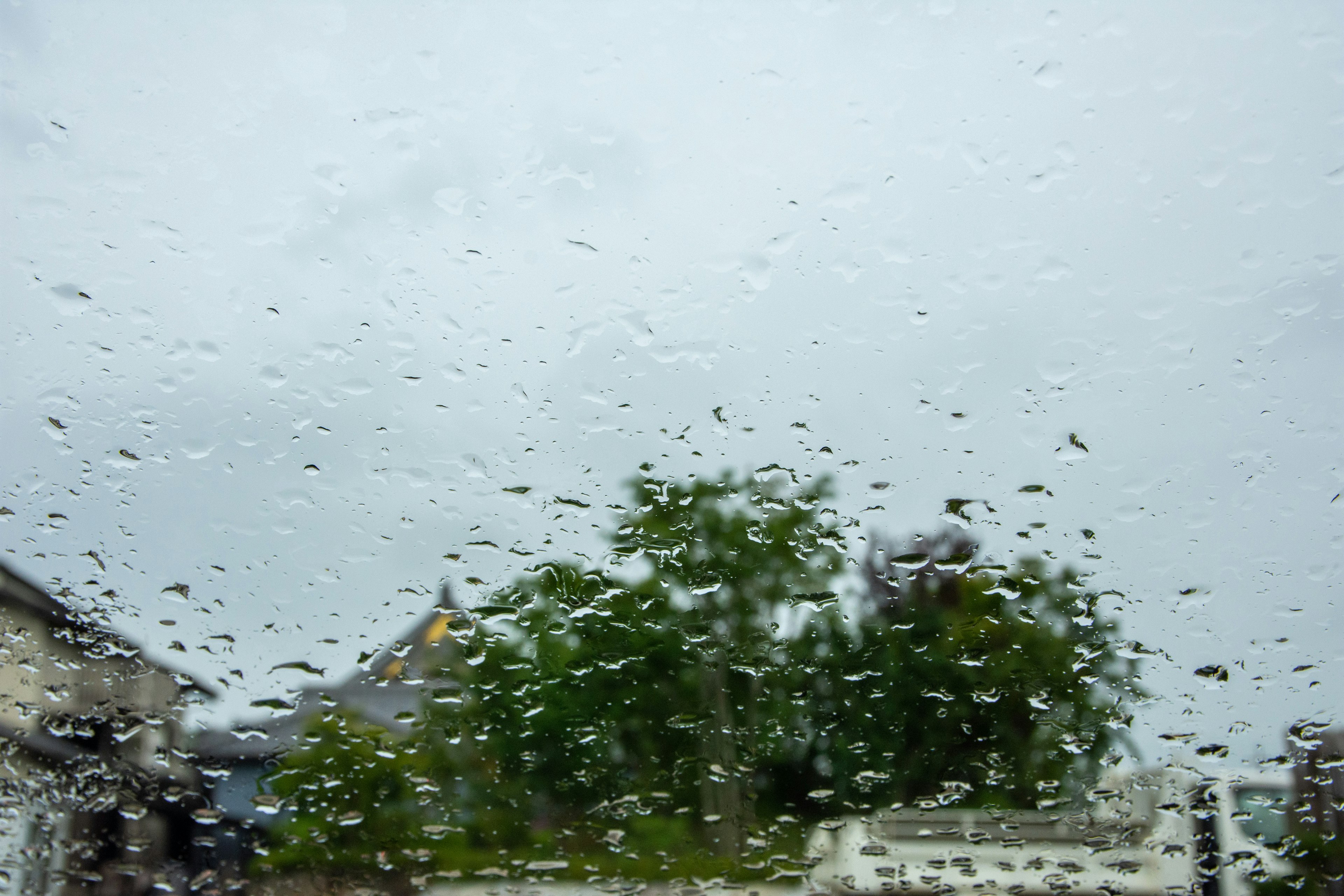 窗戶上的雨滴，背景是陰雲密布的天空和綠色樹木