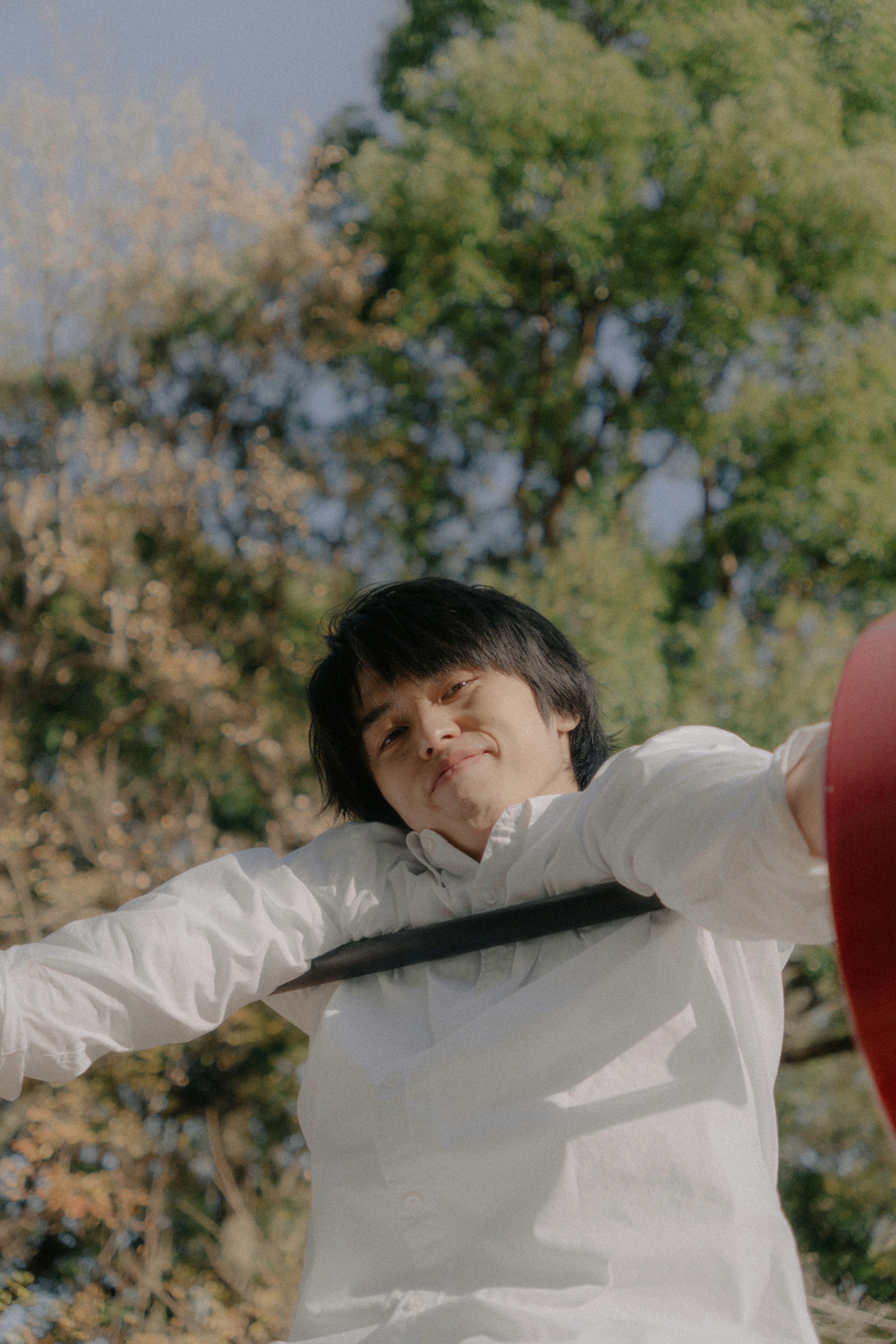 Joven con camisa blanca sosteniendo un objeto rojo al aire libre