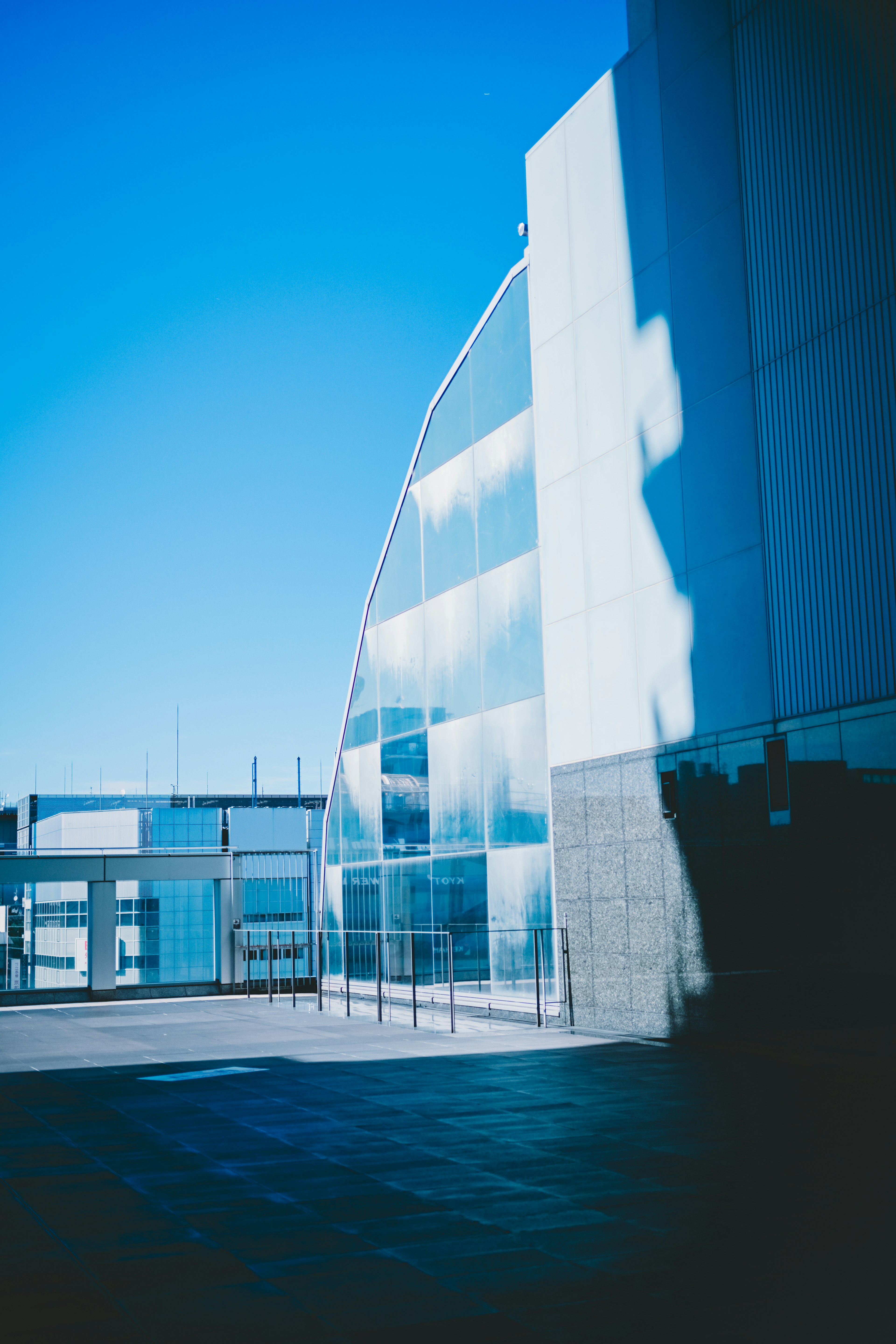 Modernes architektonisches Gebäude mit Glasfassade, die den blauen Himmel und markante Schatten reflektiert